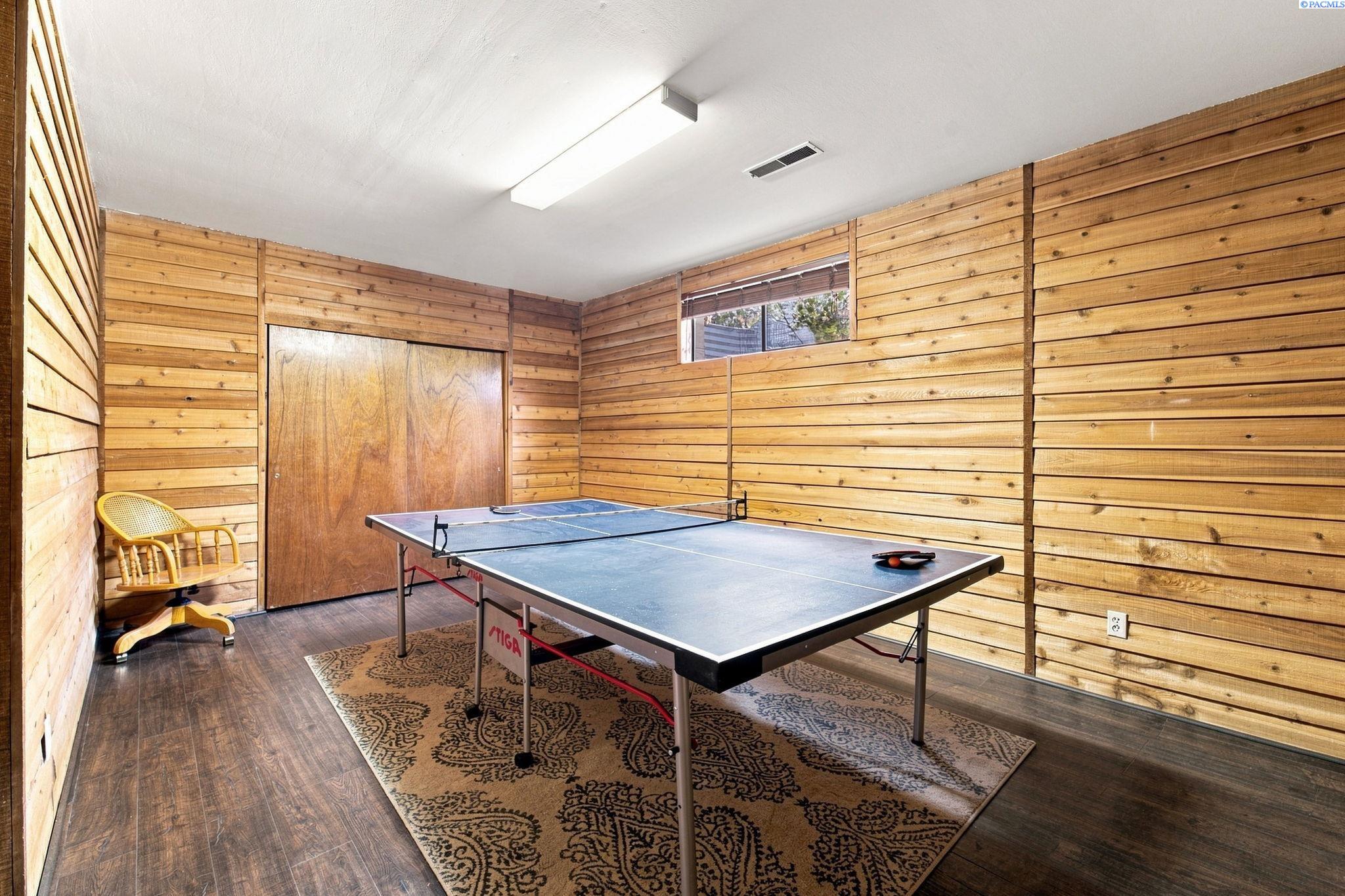 Game room with a ping-pong table, wood-paneled walls, patterned rug, and wicker chair.