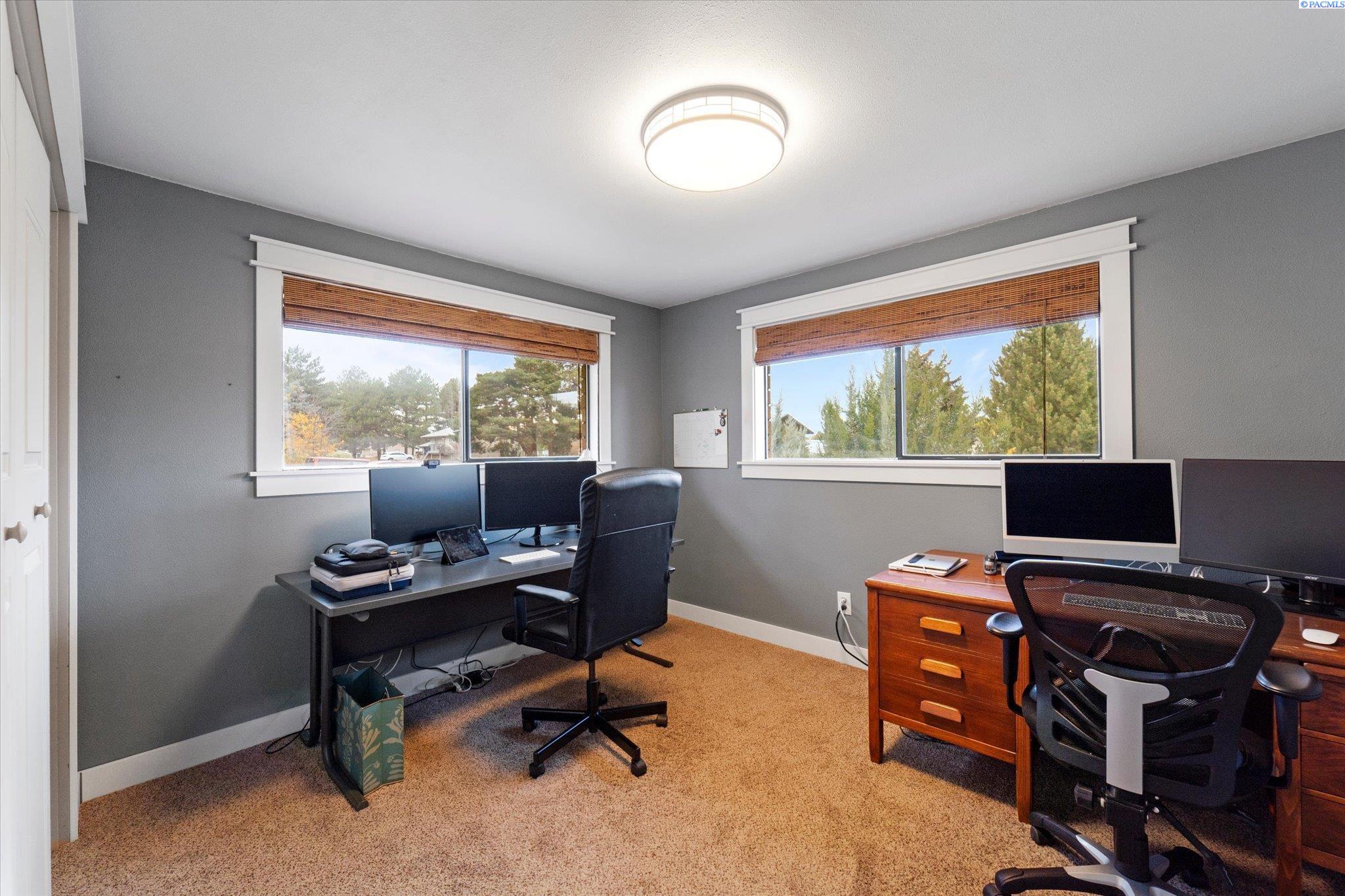 Home office with two computer workstations and windows overlooking trees.