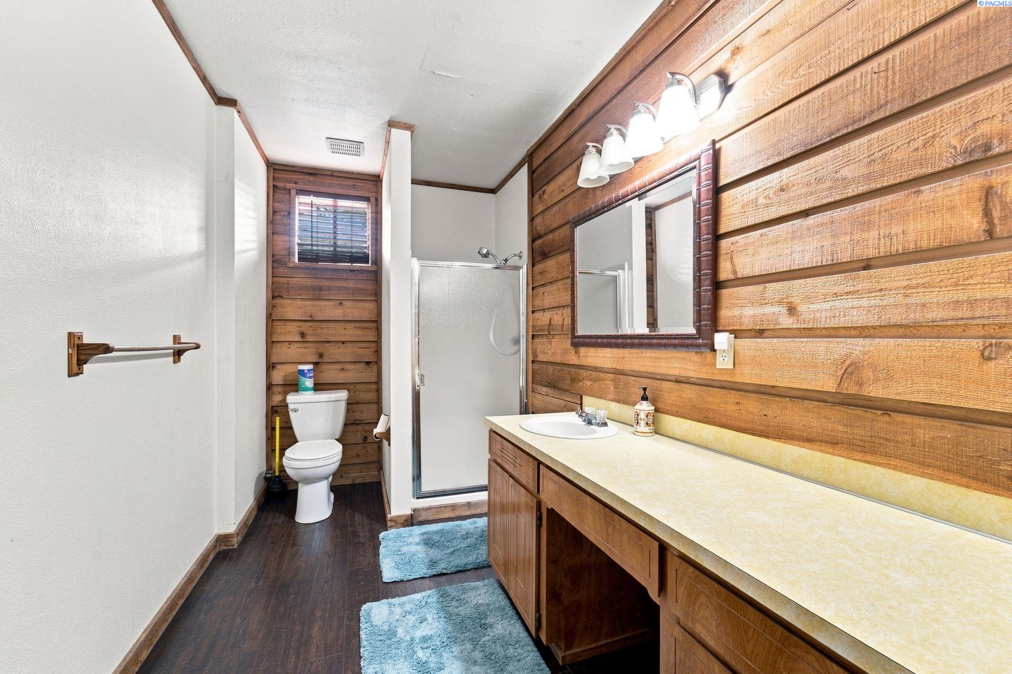 Bathroom with wood-plank walls, a long wooden vanity, glass shower, and toilet.