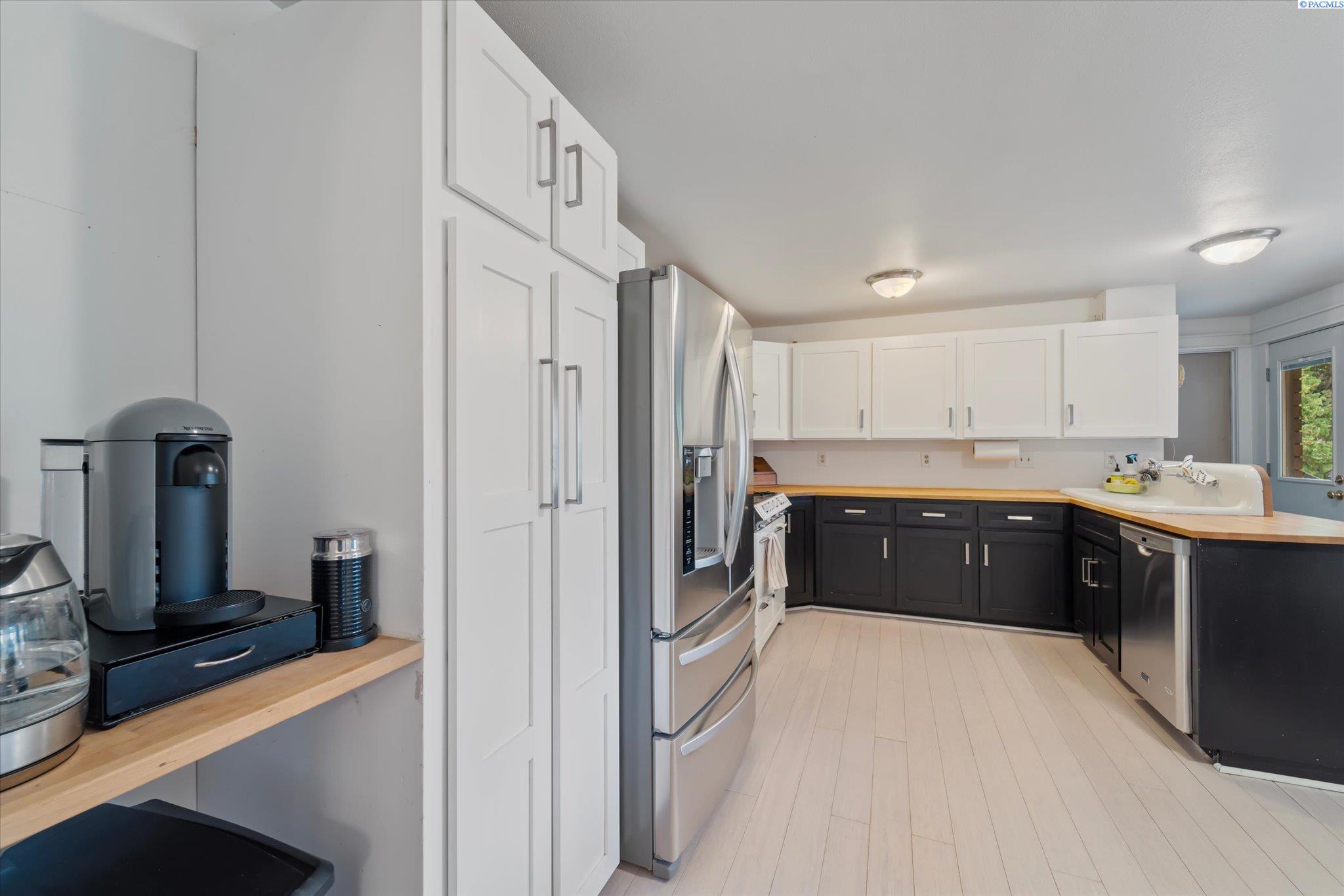 Kitchen with white upper cabinets, dark lower cabinets, light wood counters, and stainless-steel appliances.