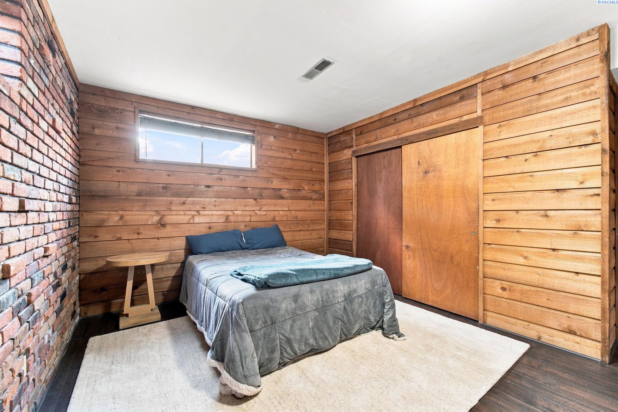 Bedroom with wood-plank walls, a brick accent wall, and a bed on a white rug.