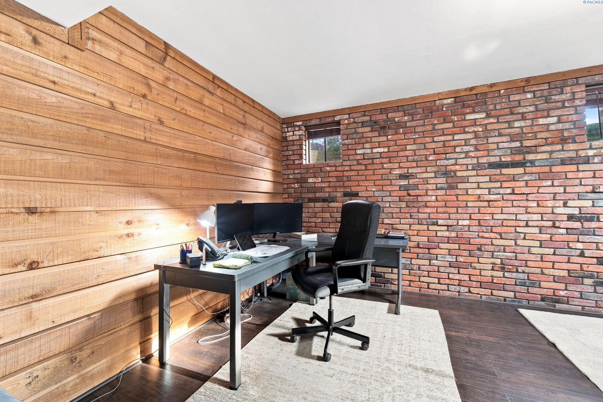 Home office with a desk and dual monitors between wood-plank and exposed brick walls.