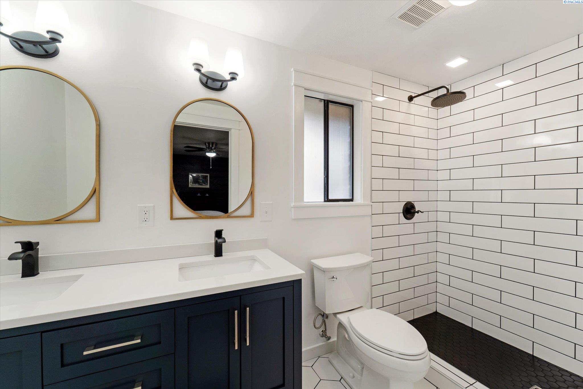 Bathroom with navy double vanity, gold-framed mirrors, and white subway-tile shower.