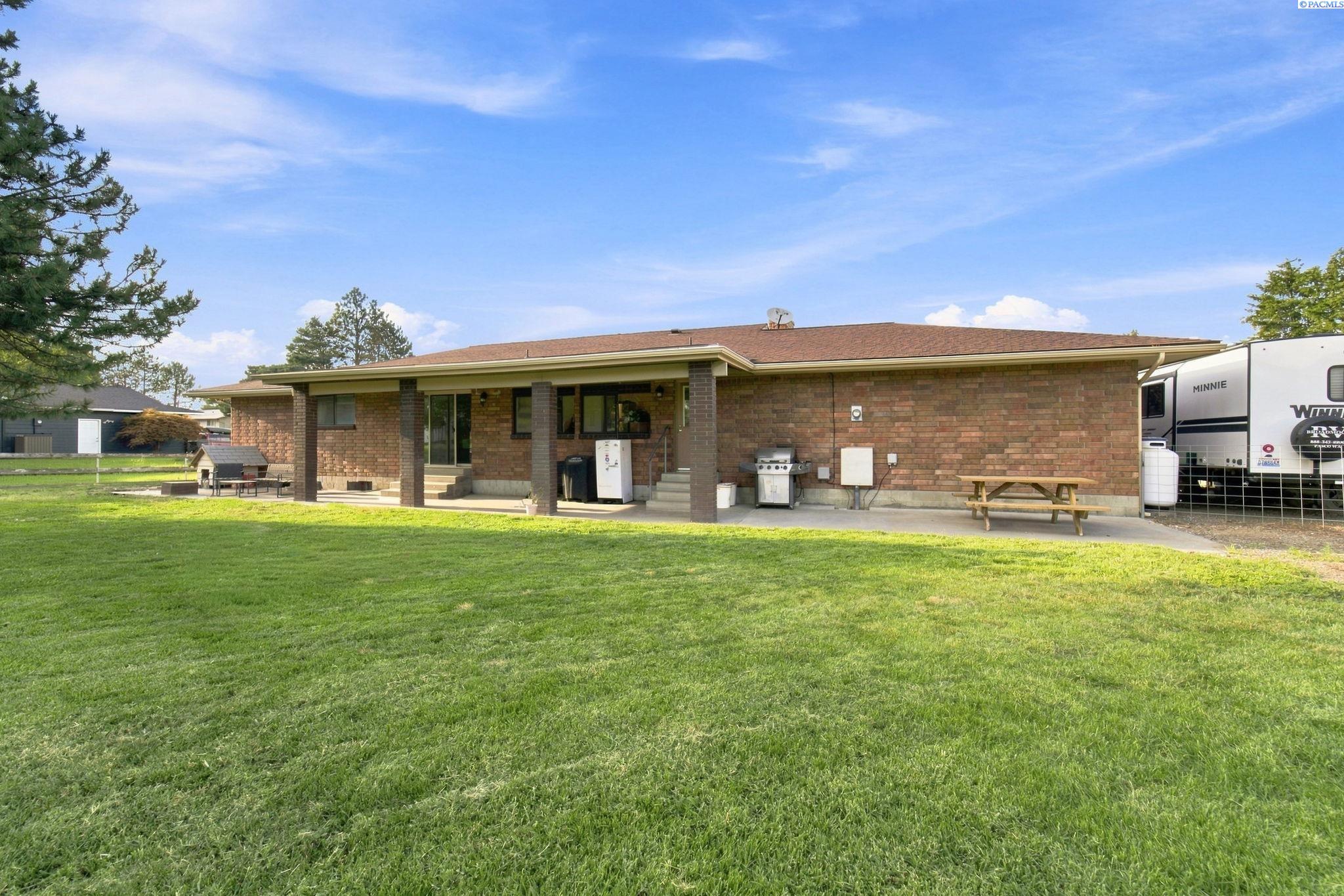 Single-story brick house with a covered patio, outdoor grill, and broad green lawn.