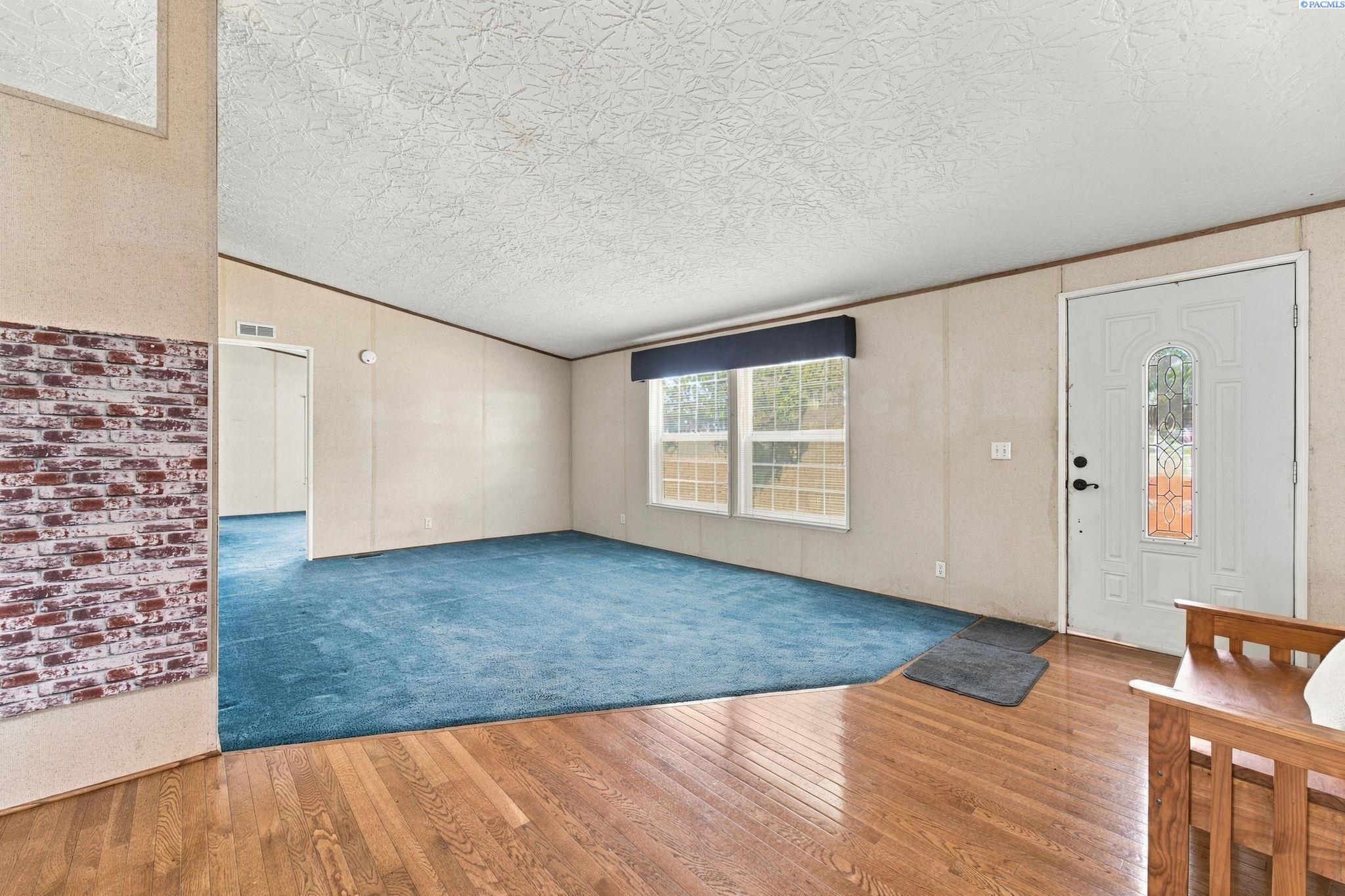 Living room with blue carpet, a large window, hardwood flooring, and a decorative-glass front door.