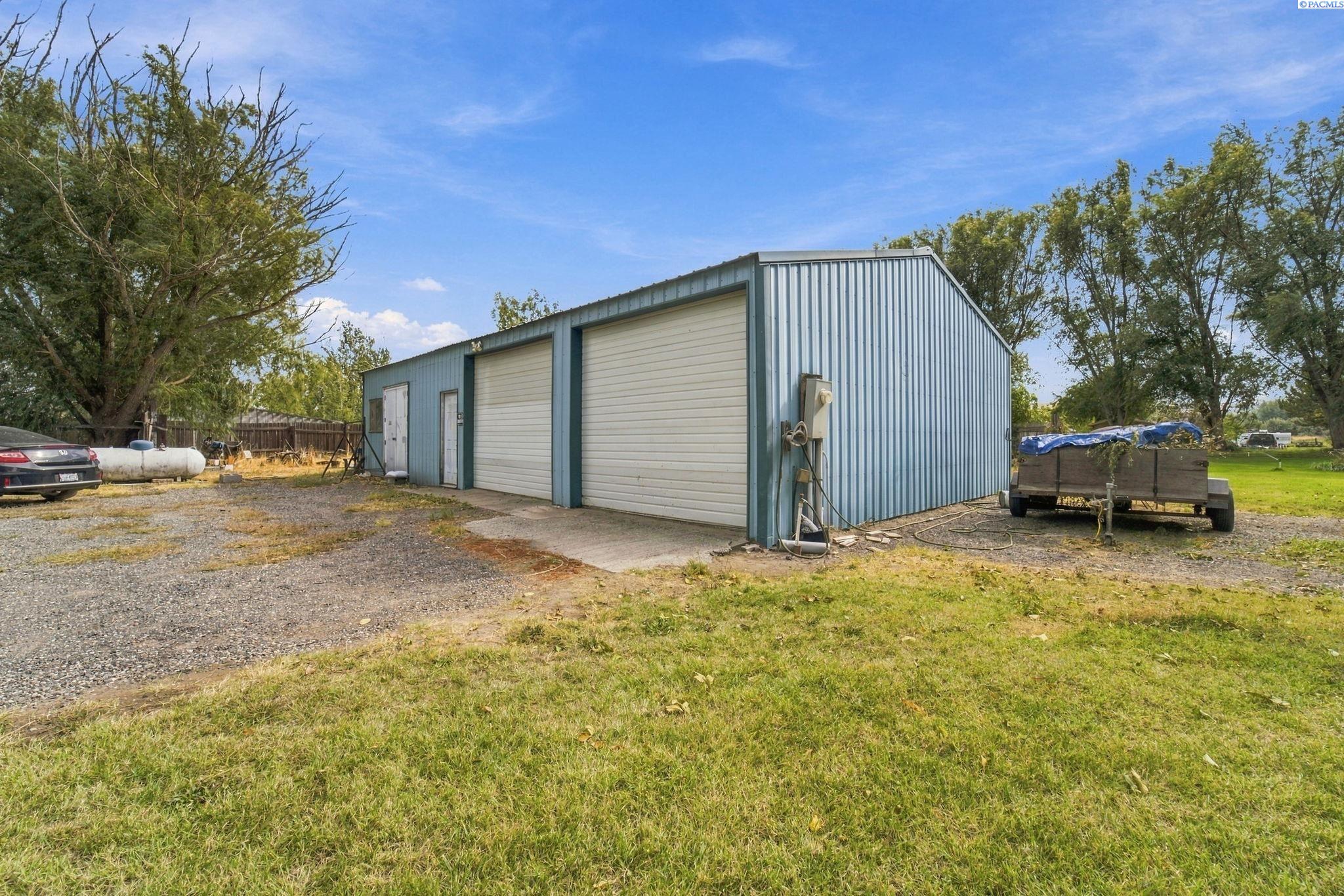 Corrugated metal workshop with two large overhead doors beside a gravel driveway and grassy yard.
