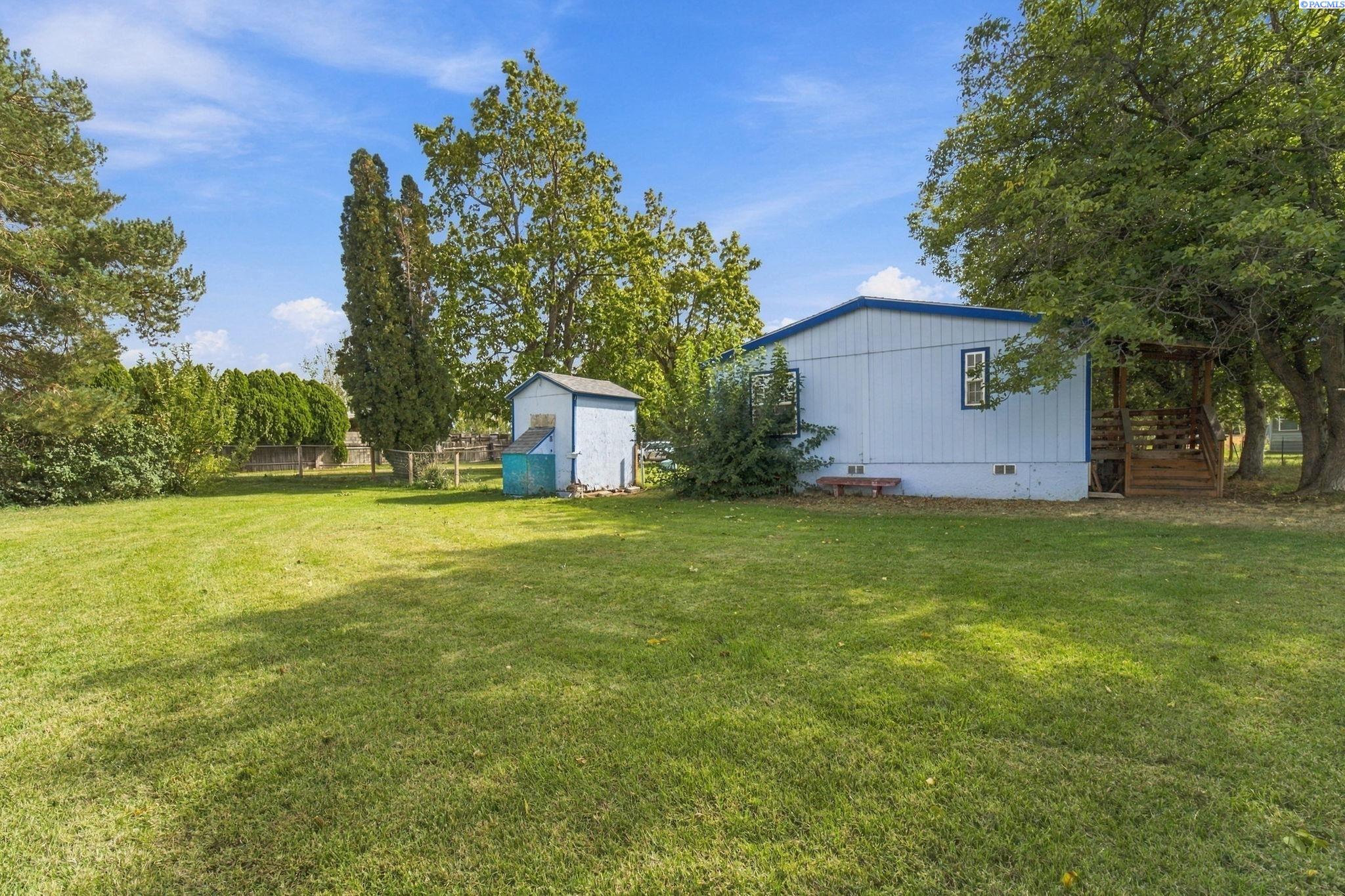 Light-blue home with a covered wooden porch and small outbuilding beyond a broad green lawn.