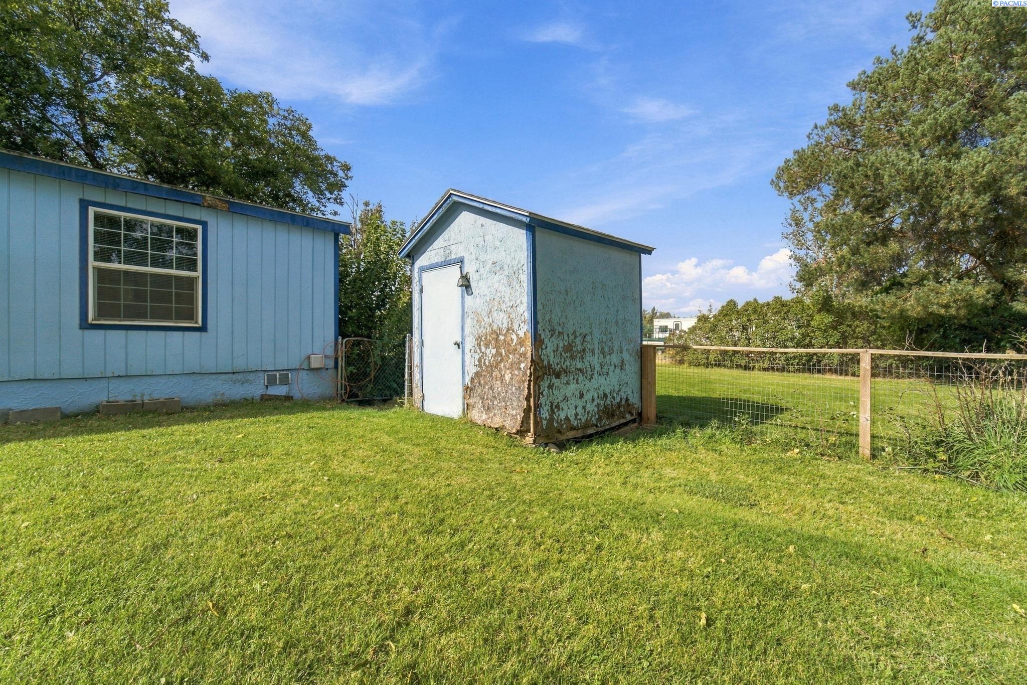 Blue-sided home beside a weathered shed in a grassy, fenced yard.