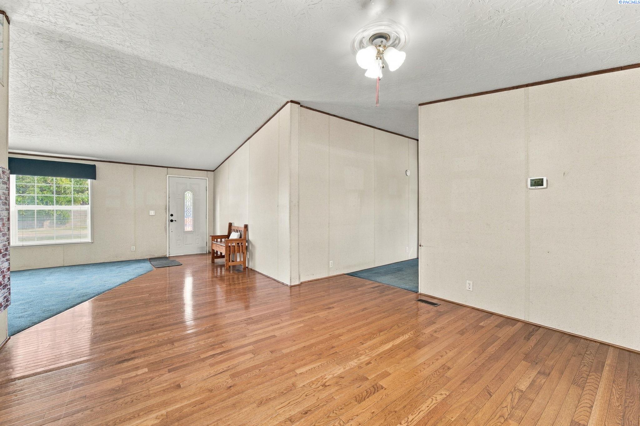 Living room with hardwood floors, a blue-carpeted area, and a small wooden chair by the front door.