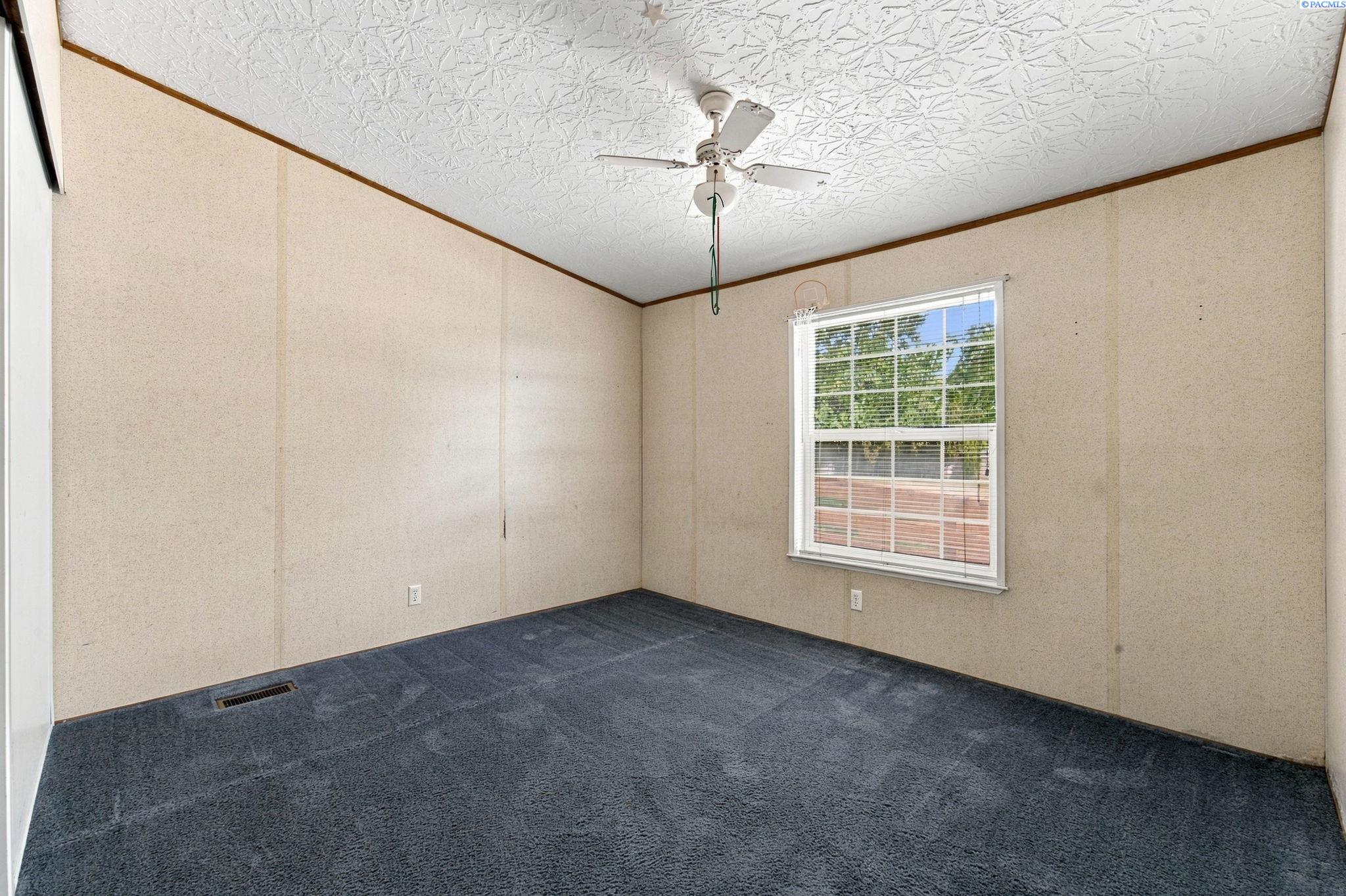Empty bedroom with dark blue carpet, beige walls, and a window with white blinds.