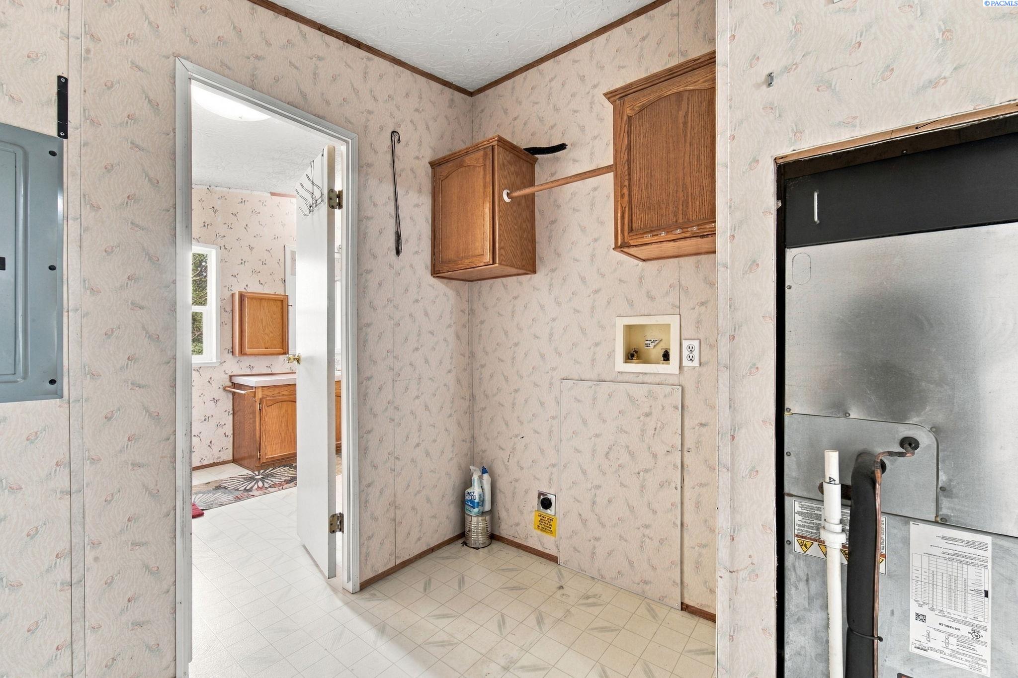 Utility room with wood cabinets, tiled floor, and exposed mechanical equipment beside a bathroom doorway.