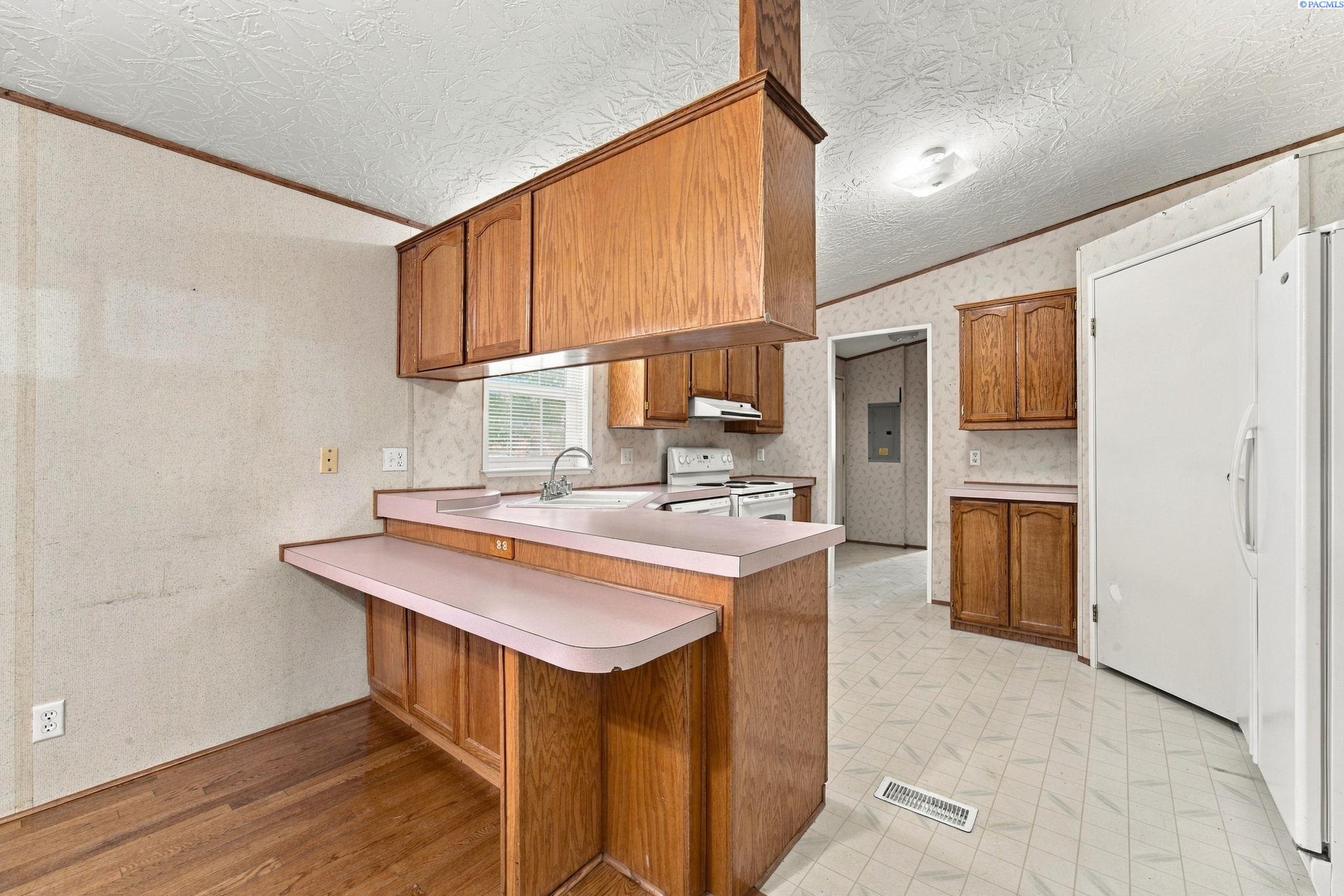 Kitchen with oak cabinets, pink countertops, a breakfast bar, and white appliances.