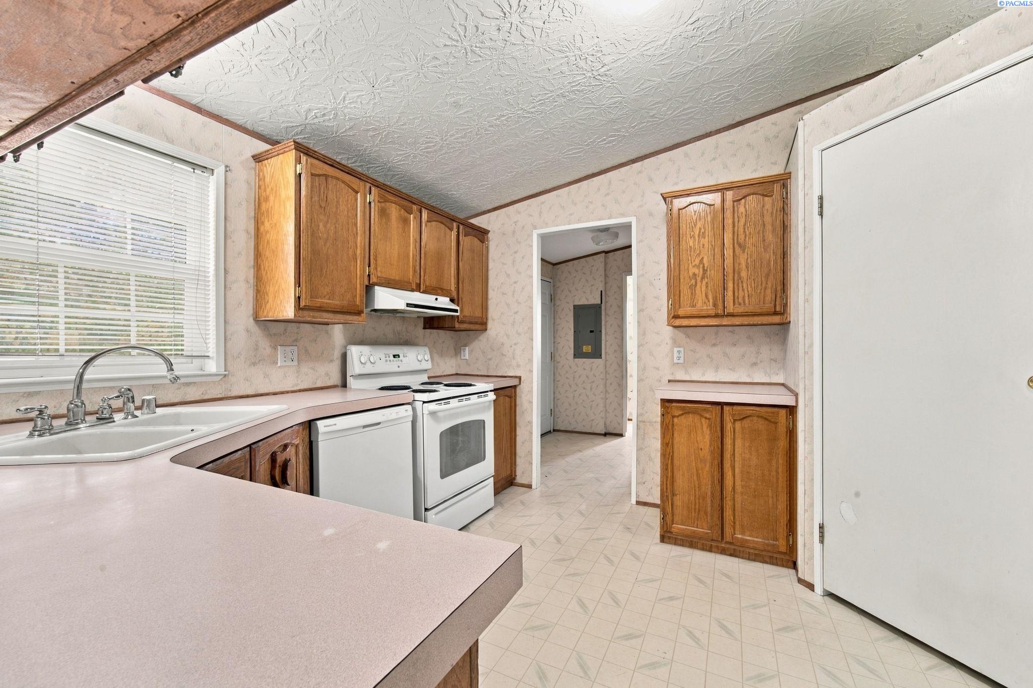 Kitchen with oak cabinets, pale countertops, a sink beneath the window, and an electric range.