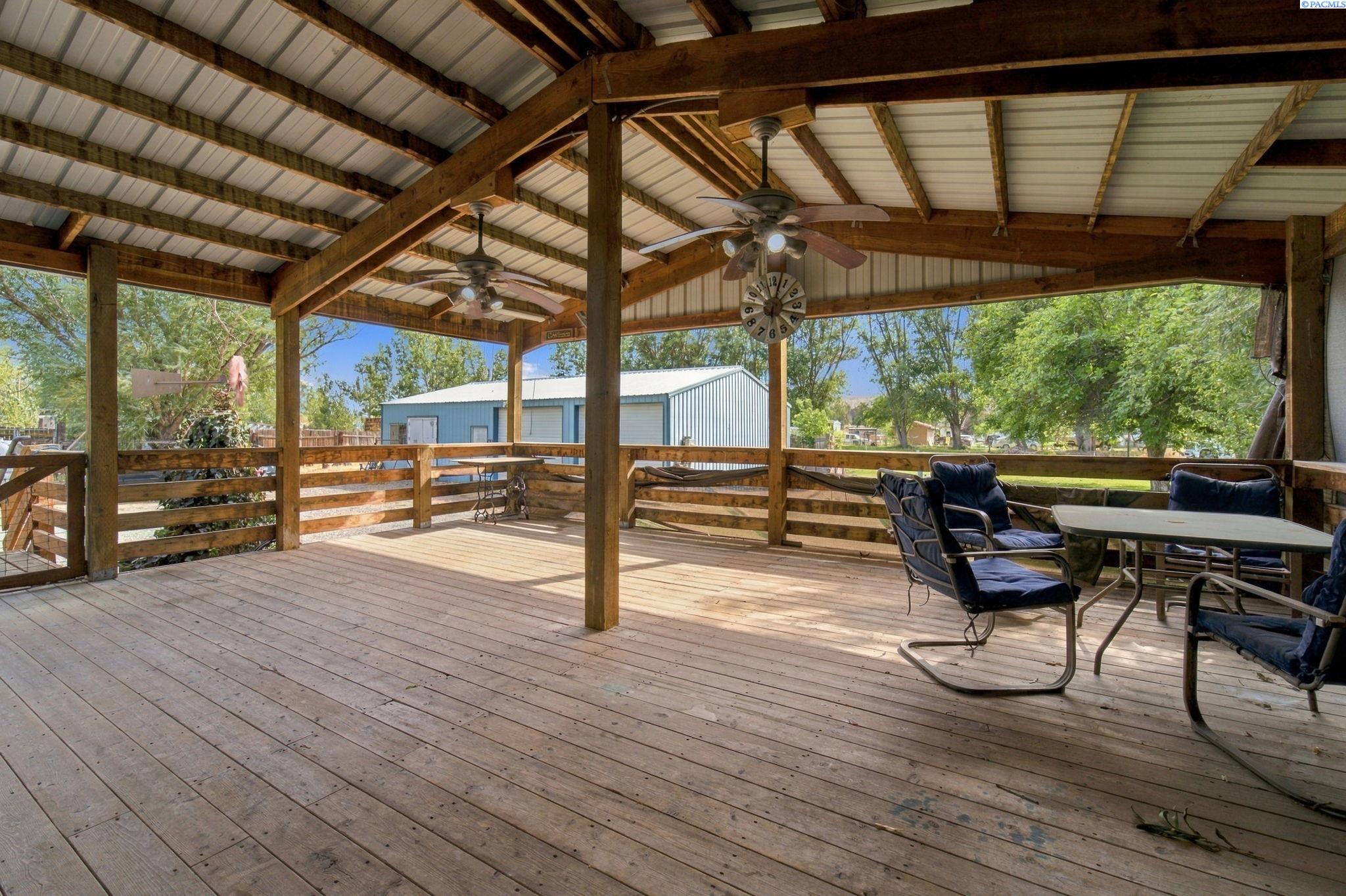 Covered timber patio with ceiling fans, a wall clock, and cushioned outdoor seating.