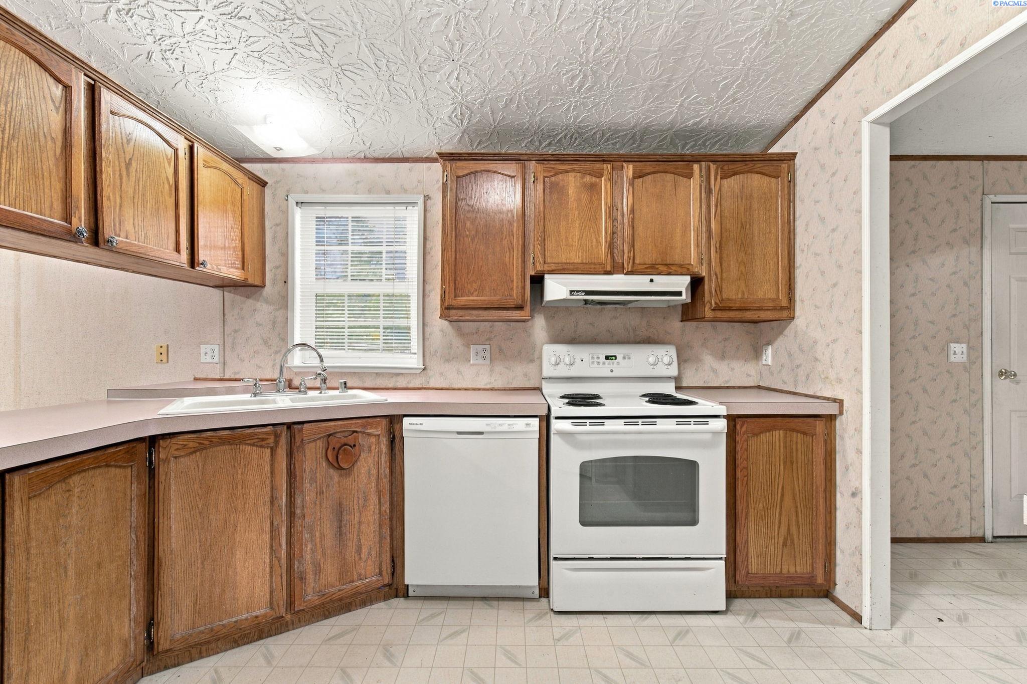 Kitchen with honey-brown wood cabinets, pale countertops, a white electric range, and a dishwasher.