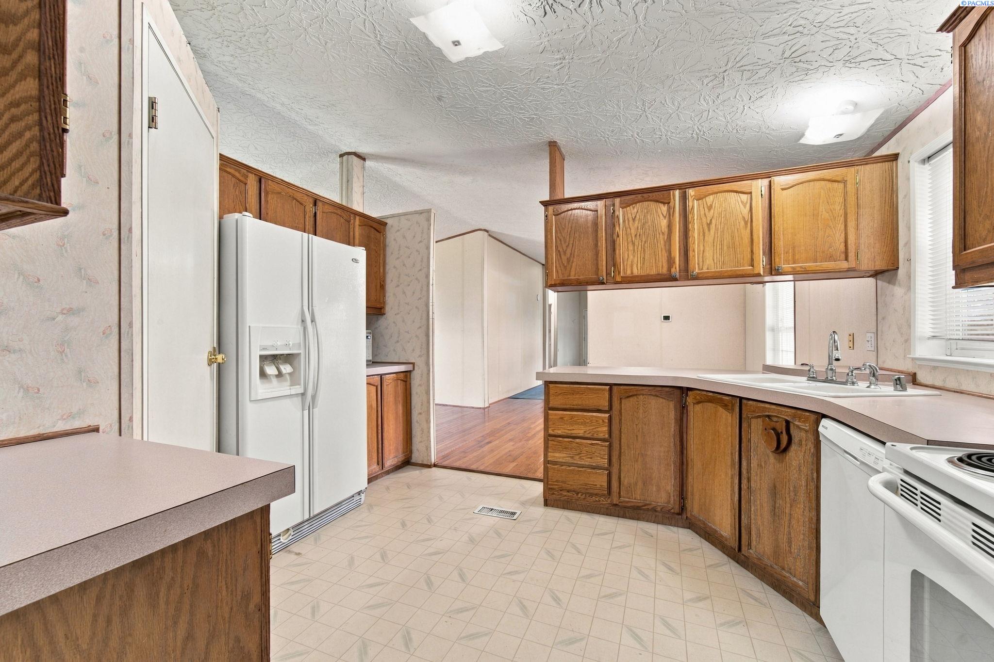 Kitchen with wood cabinets, white appliances, a double sink, and an adjoining room with hardwood floors.