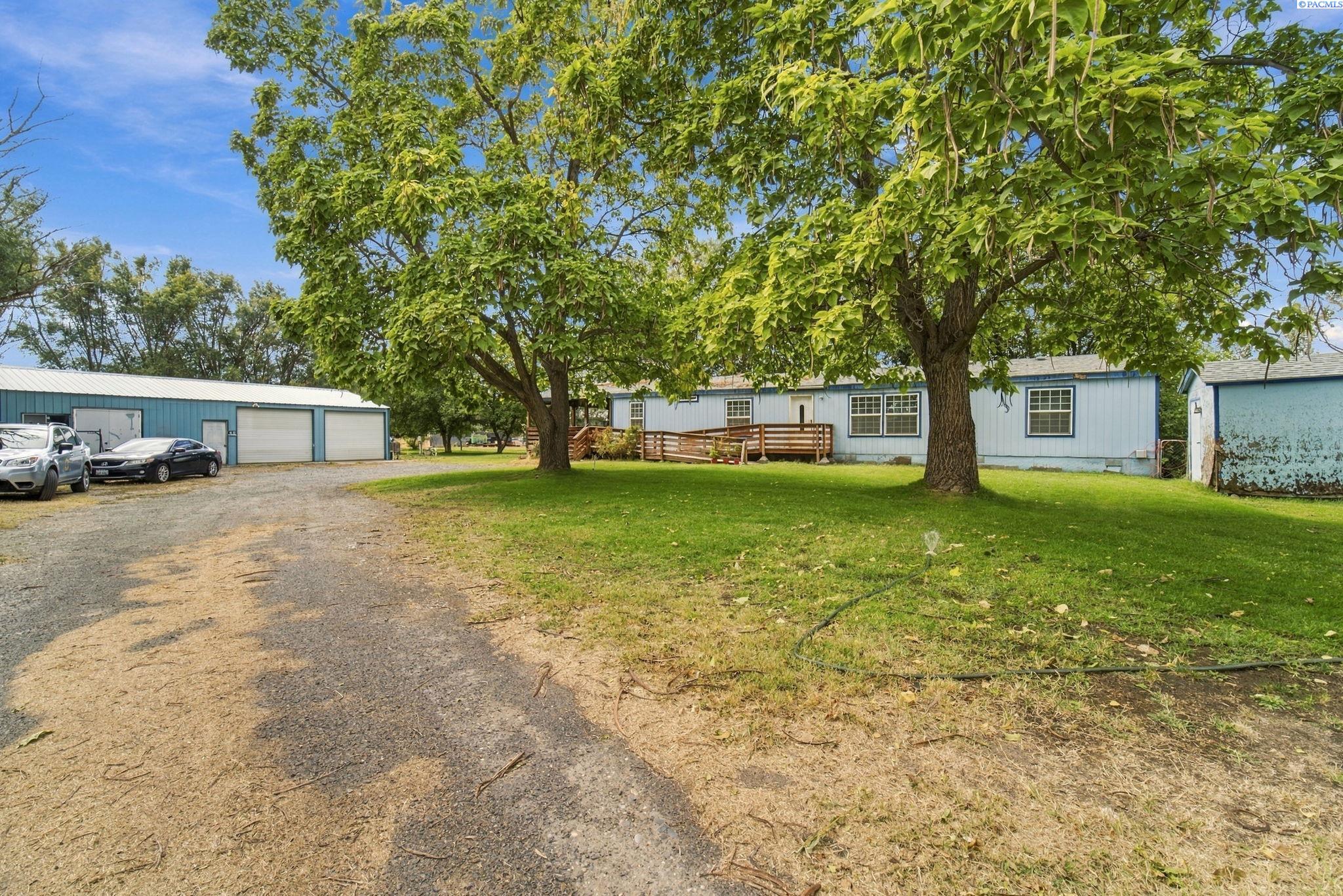 Light-blue home and wooden deck beneath mature trees, with a broad lawn and detached garage.