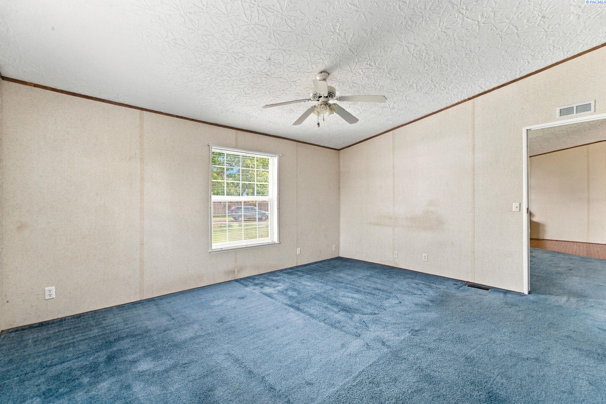 Empty room with blue carpet, a ceiling fan, and a window overlooking the yard.