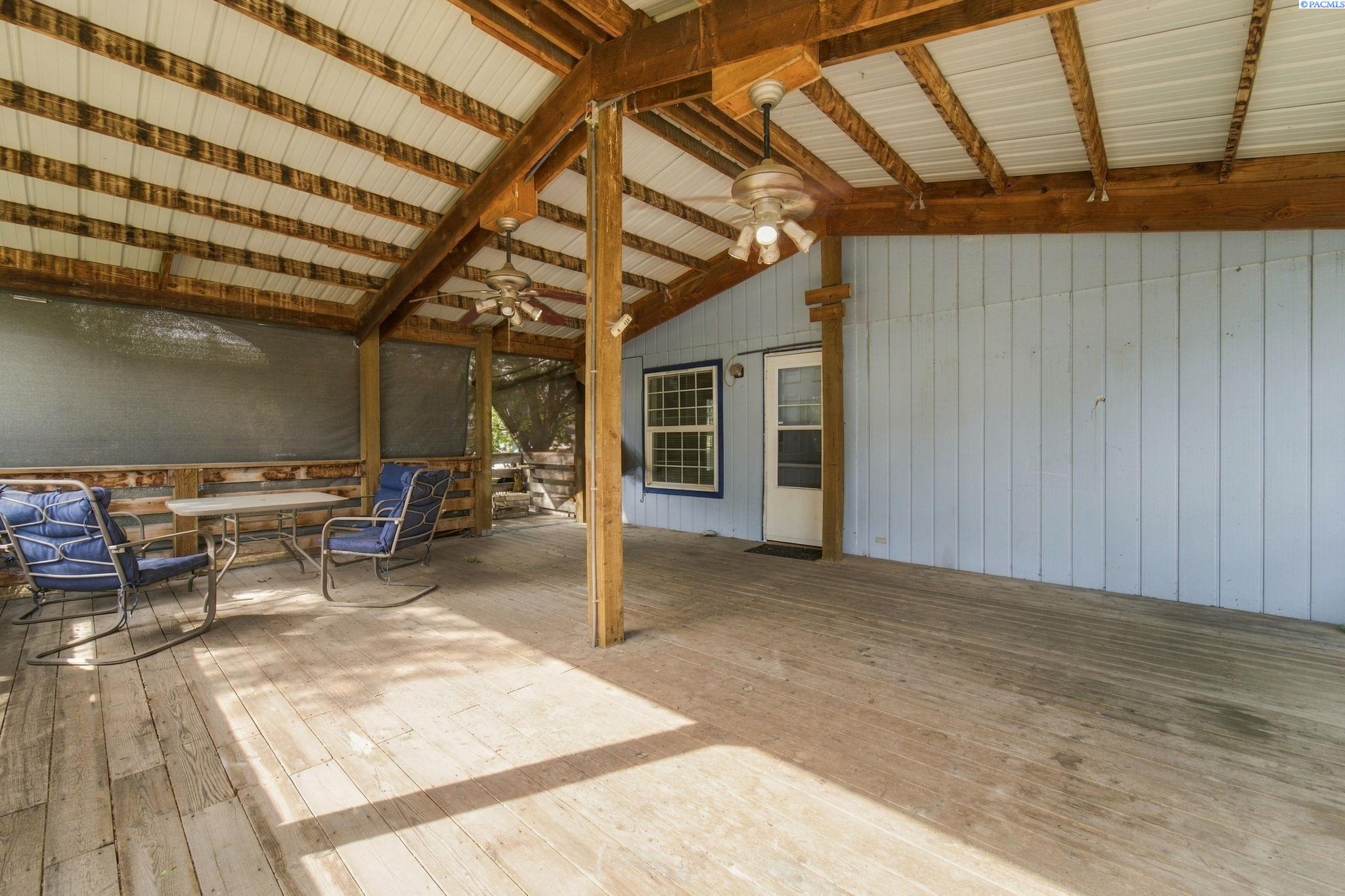 Covered wooden porch with exposed beams, ceiling fans, and blue outdoor seating.
