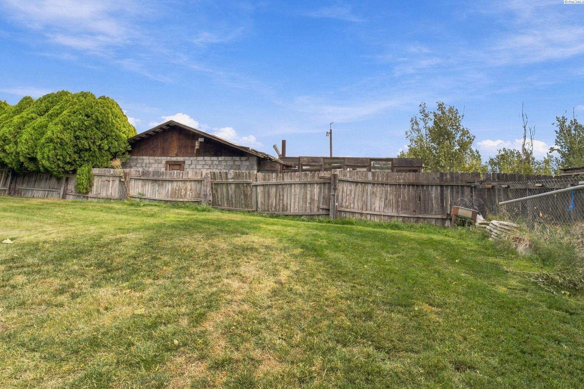 Grassy backyard with mature trees, a weathered wooden fence, and a low outbuilding.