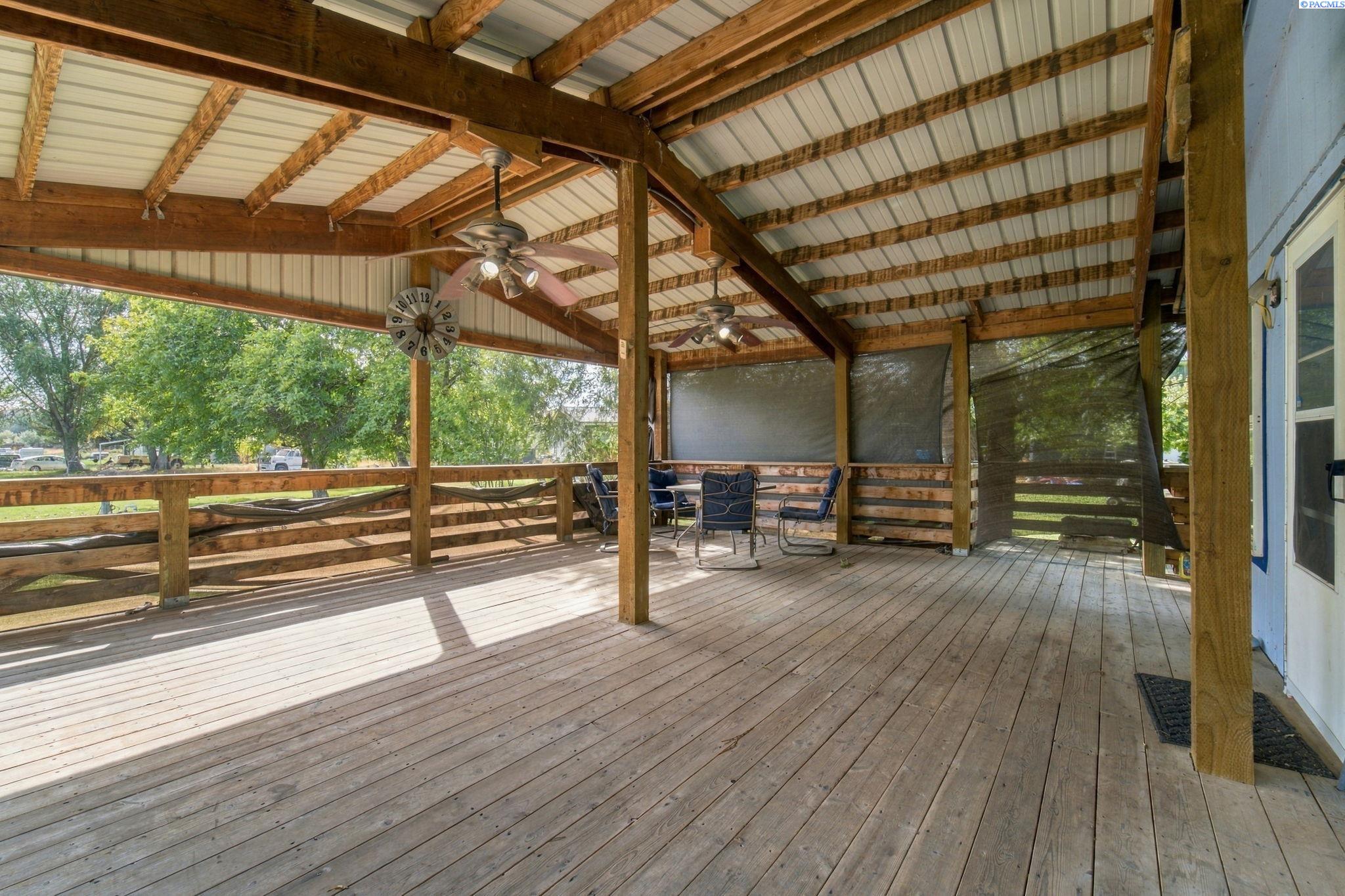 Covered wooden deck with exposed beams, ceiling fans, screened sides, and outdoor seating.