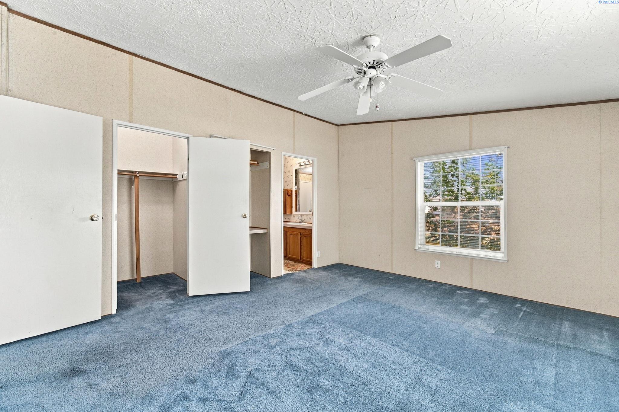 Empty bedroom with blue carpet, an open closet, and a window overlooking trees.