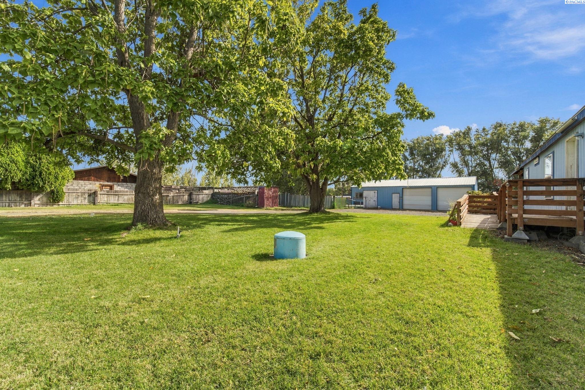 Spacious backyard with mature trees, a wooden deck, and a detached blue garage.