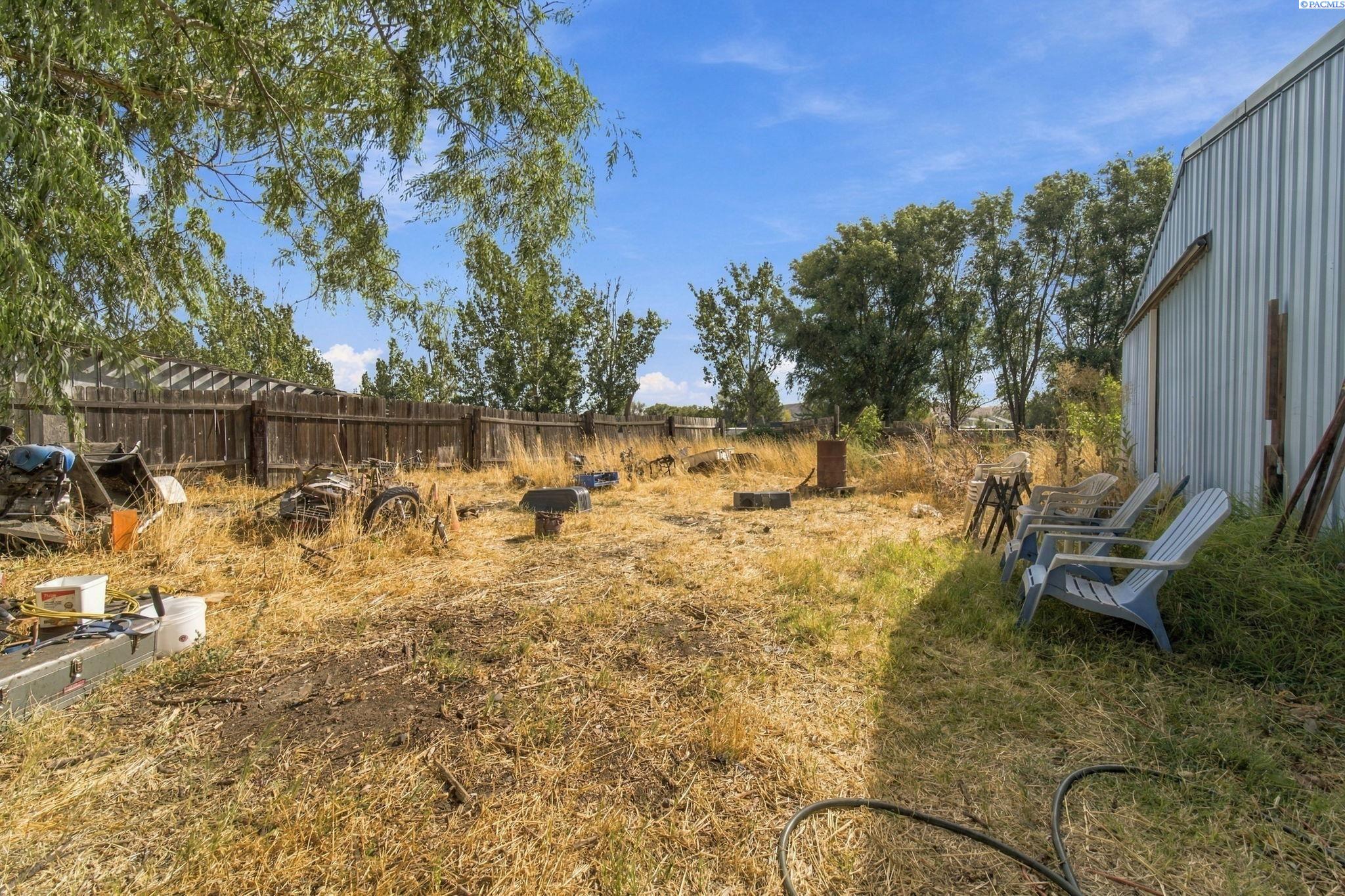 Dry, fenced yard beside a metal outbuilding, with scattered equipment and chairs along the wall.