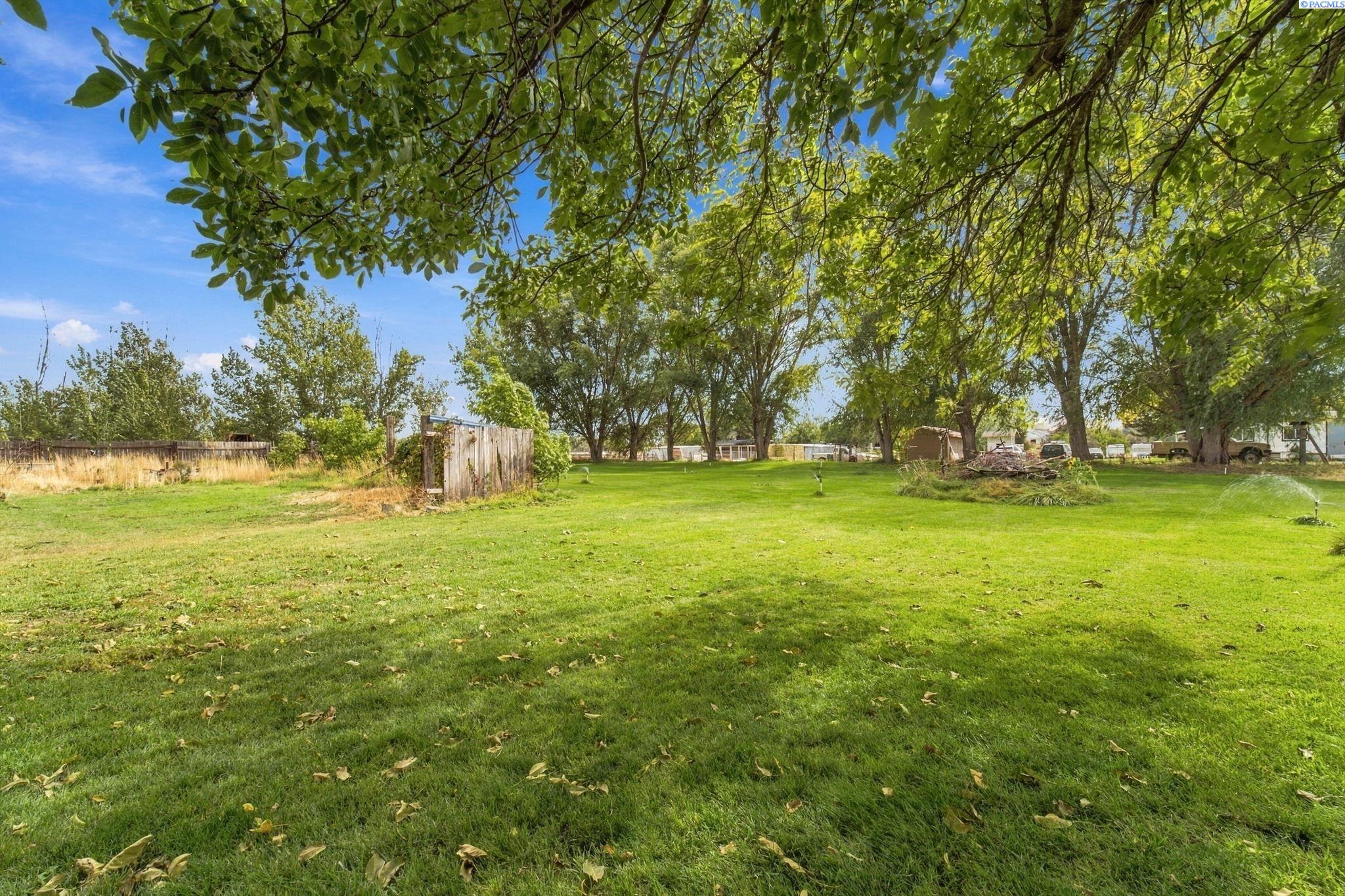 Expansive lawn beneath mature shade trees, with sprinklers and outbuildings in the distance.
