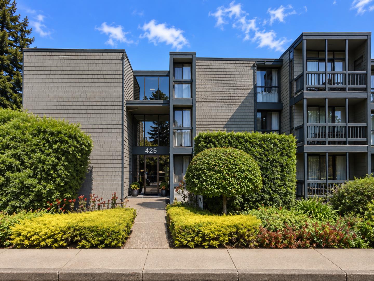 Multi-story apartment building with gray shingle siding, balconies, and landscaped entrance marked 425.