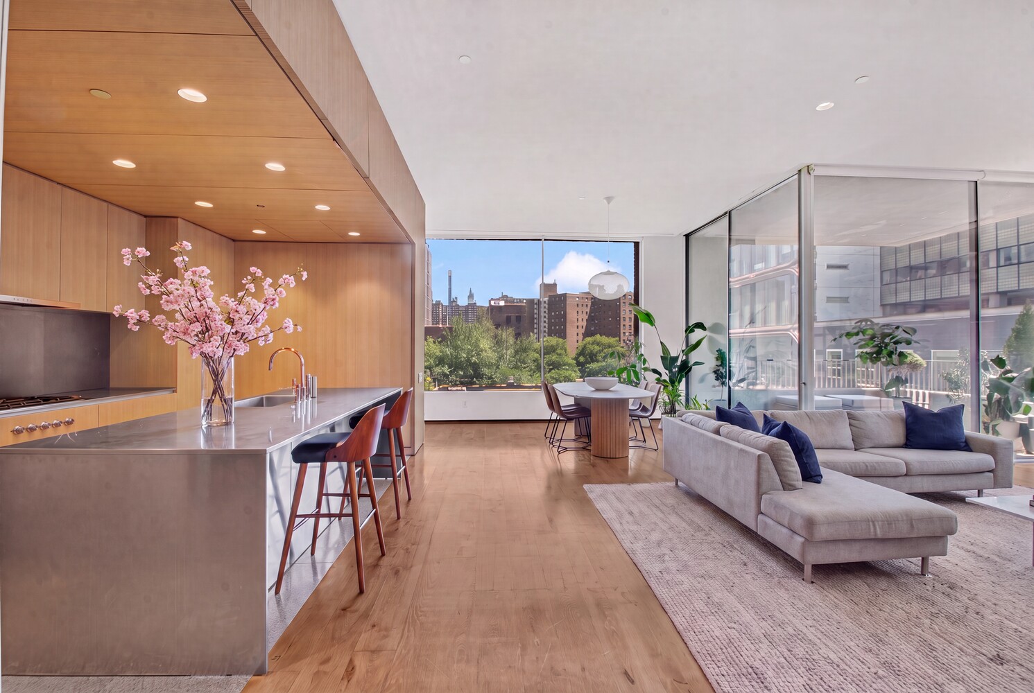 Open-plan Manhattan apartment with a wood-paneled kitchen, dining area, and floor-to-ceiling city-view windows.