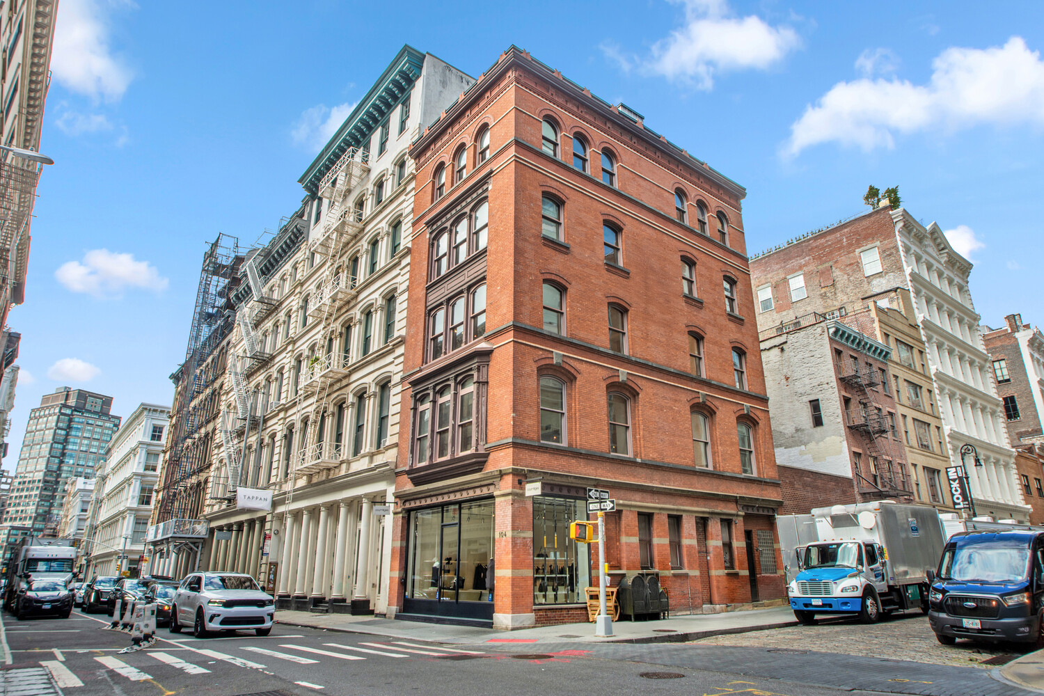 Red-brick corner building at 104 Grand Street with arched upper windows and ground-floor storefronts.