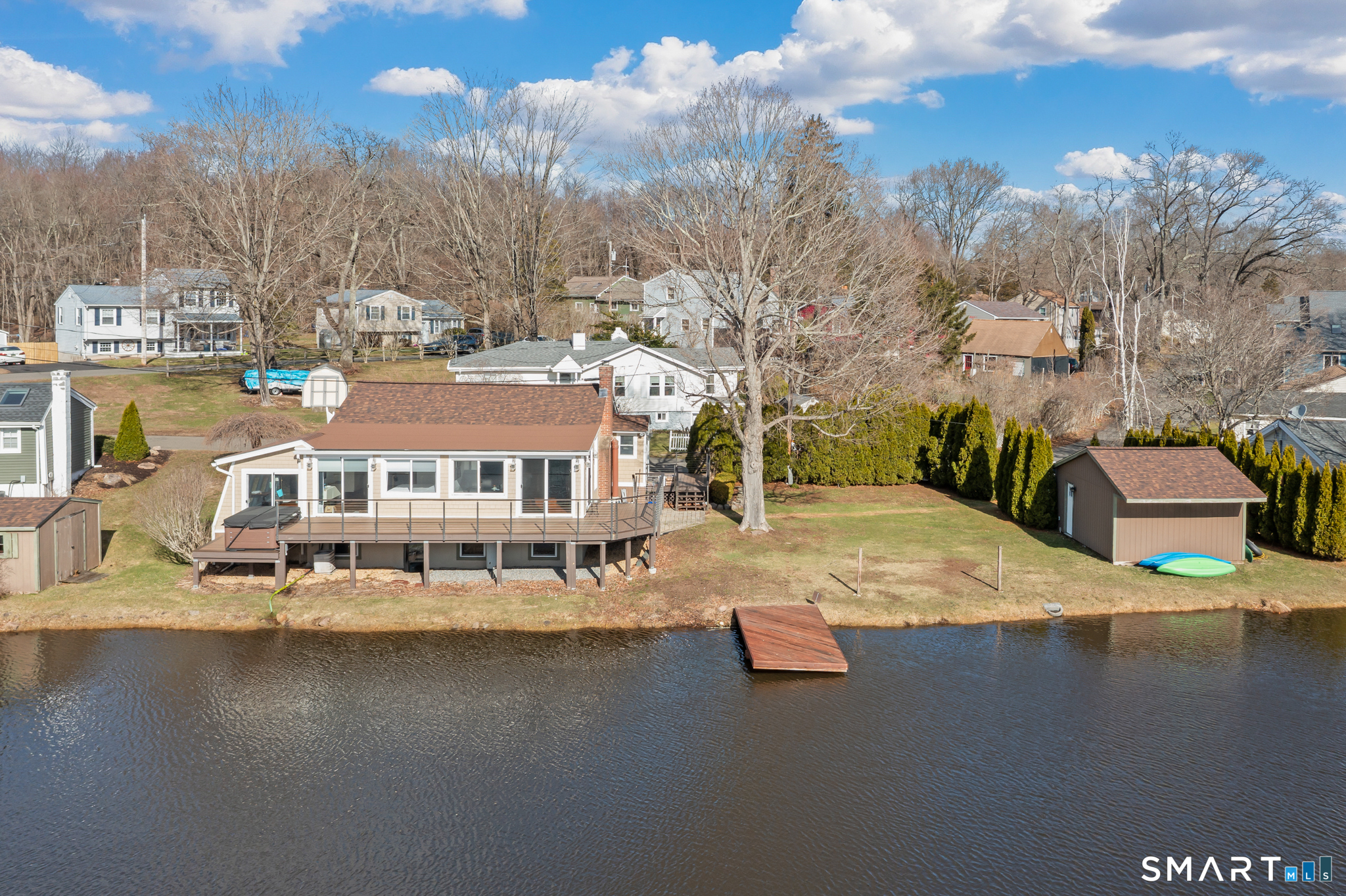 Waterfront home with a broad deck, small dock, and detached shed.