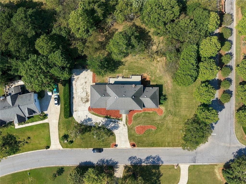 Aerial view of a single-story home with a curved driveway, landscaped lawn, and mature trees.