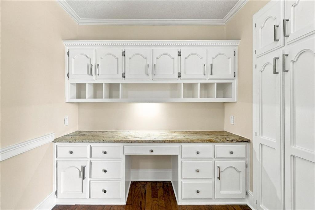 Built-in desk with stone countertop, white cabinets, and dark hardwood flooring.