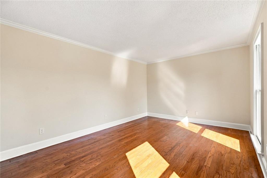 Empty room with hardwood floors and sunlight streaming through a tall glass door or window.