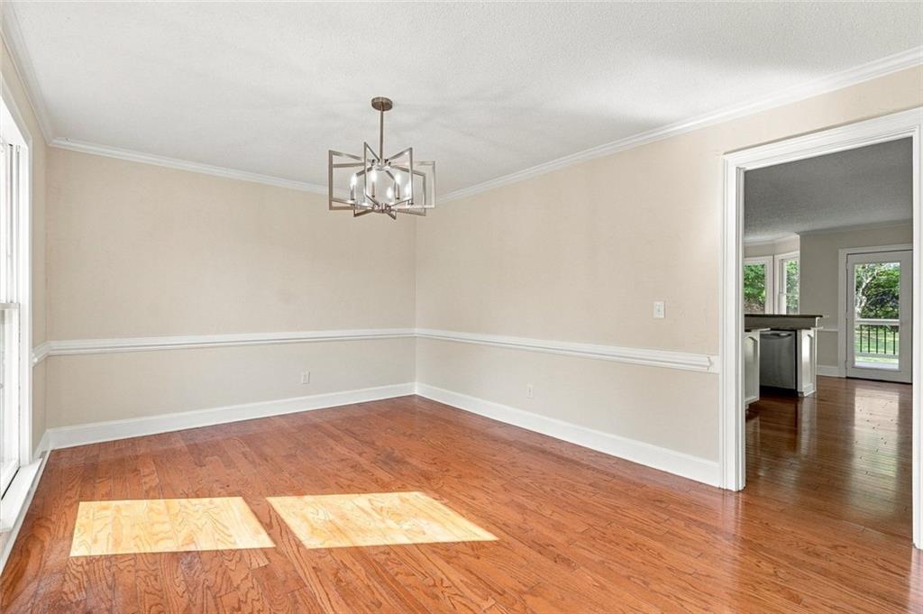 Empty dining room with hardwood floors, a geometric chandelier, and a wide opening to the kitchen.
