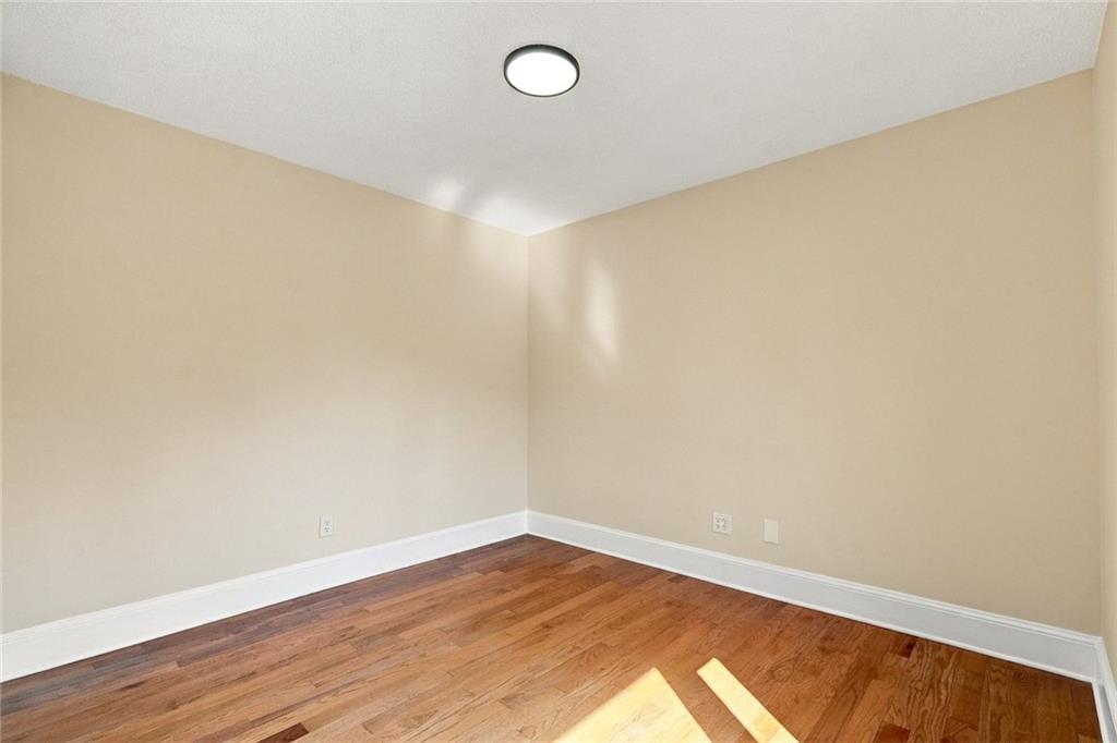 Empty room with reddish hardwood floors, beige walls, and sunlight across the floor.