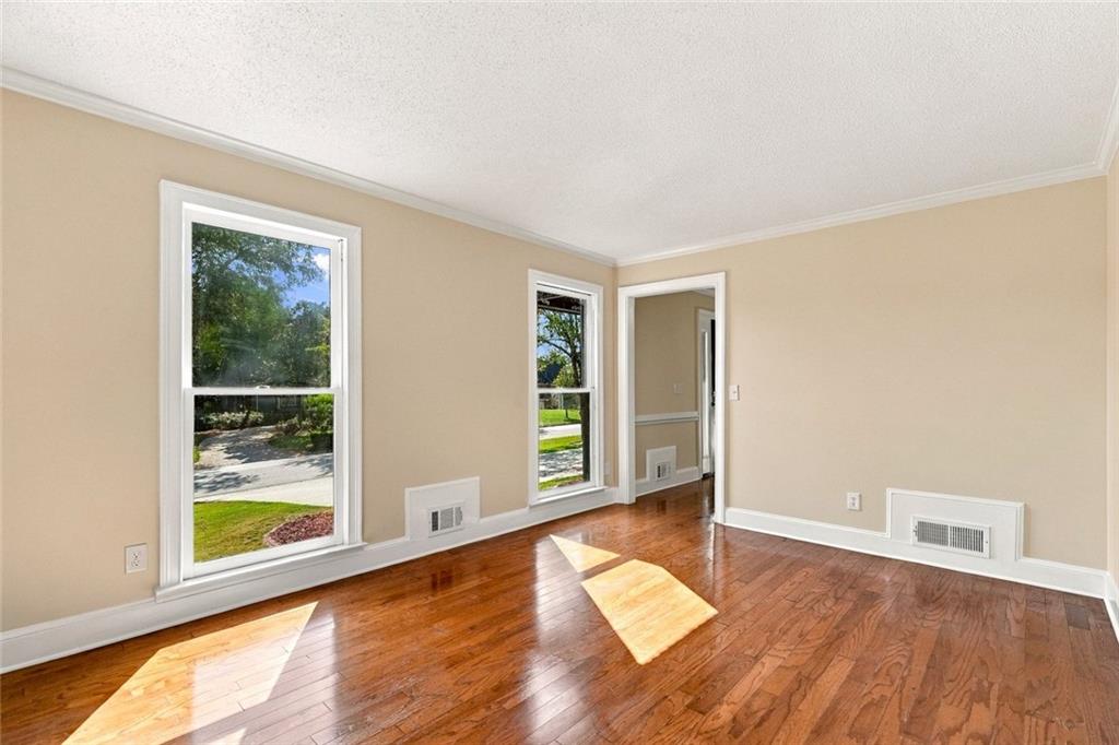 Empty room with polished hardwood floors, beige walls, and three tall windows.