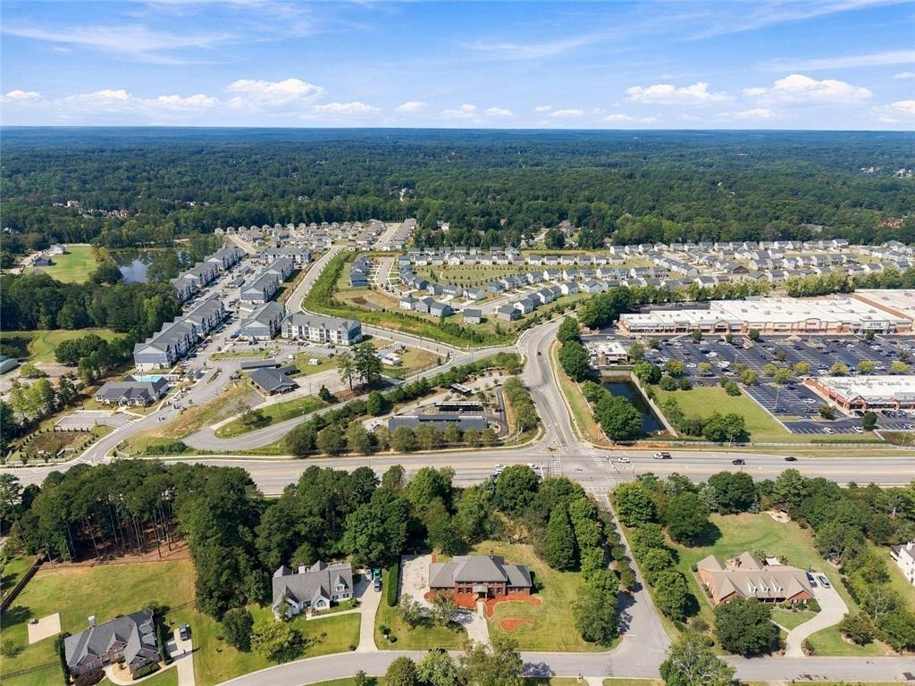 Aerial view of homes and a shopping center beside a wooded landscape.