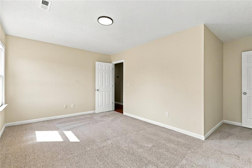 Empty bedroom with beige walls, carpet, and sunlight on the floor.