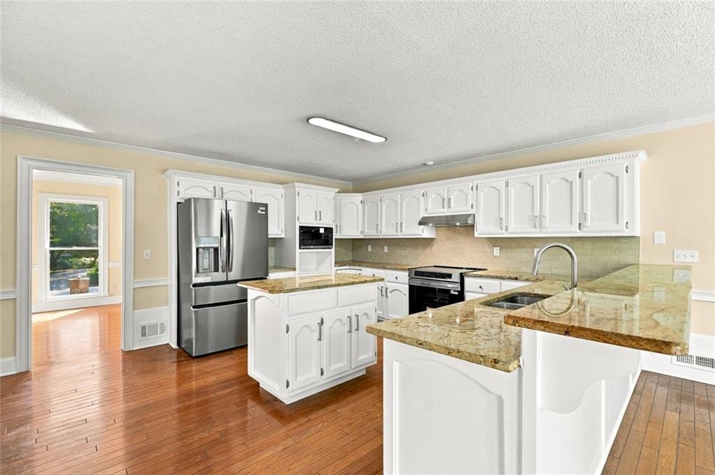 Kitchen with white cabinets, granite island, stainless steel appliances, and hardwood flooring.