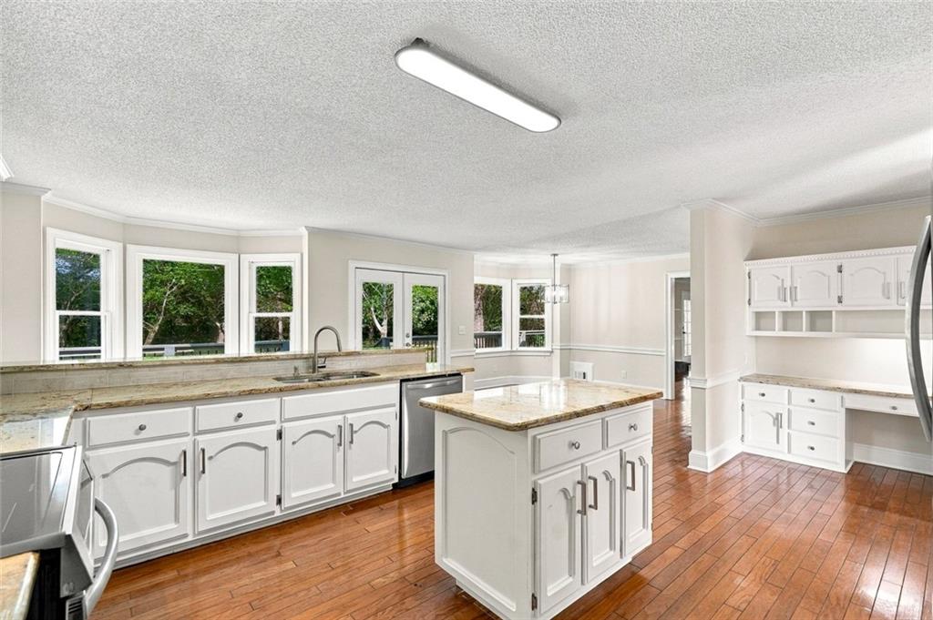 Kitchen with white cabinetry, granite island, hardwood floors, and large windows.