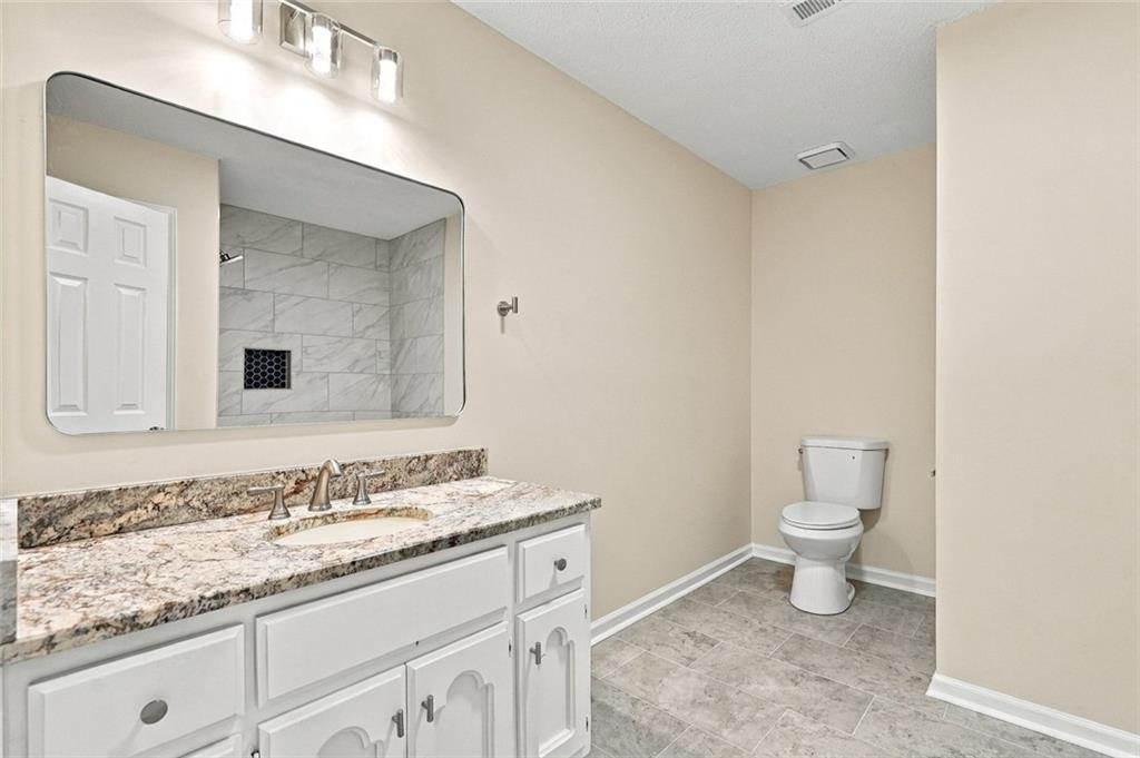Bathroom with a white vanity, marbled countertop, and mirror reflecting a gray tiled shower.