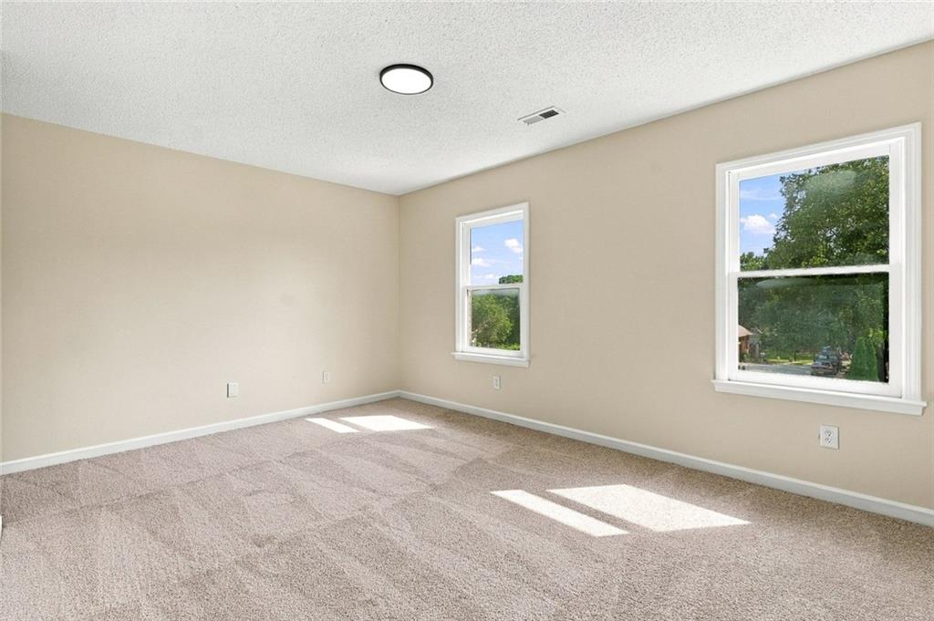 Empty carpeted room with beige walls and two windows.