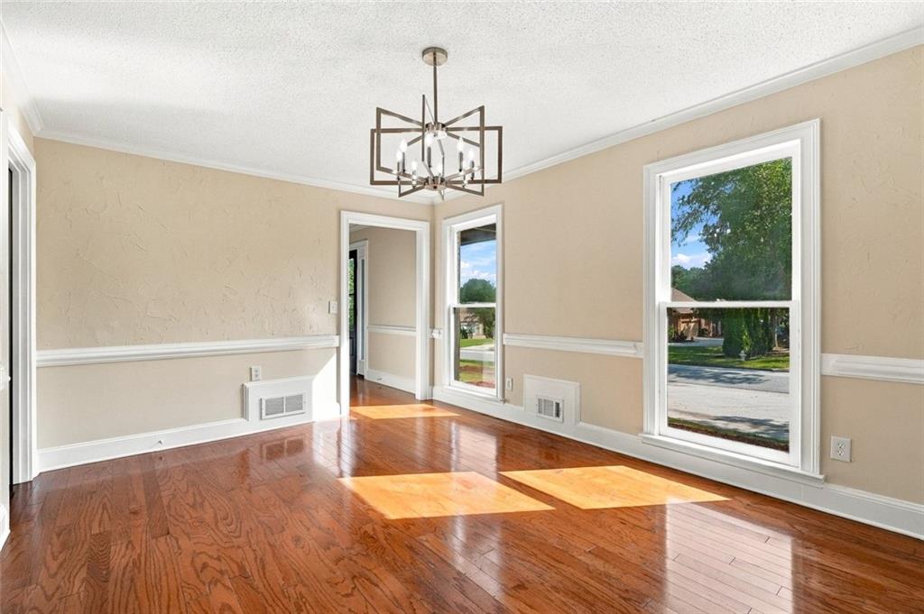 Empty room with polished hardwood floors, tall windows, and a geometric chandelier.