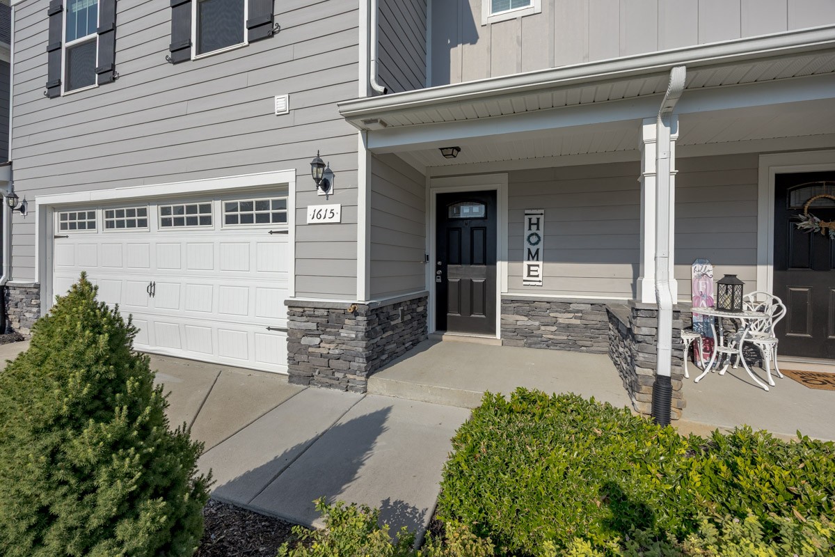 Gray two-story home with a white garage door, stone-accented covered entry, and landscaped shrubs.