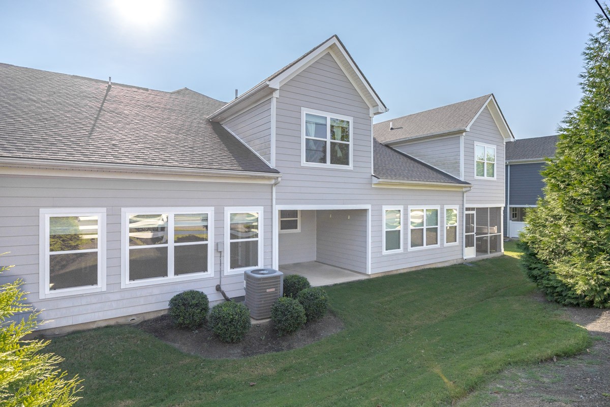 Gray two-story home’s rear exterior with a covered patio, white-trimmed windows, and lawn.