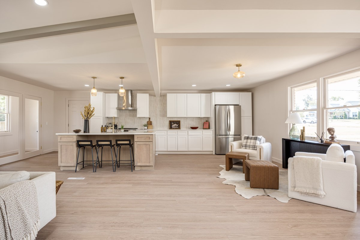 Open-plan kitchen and living area with a large island, white cabinetry, and bright window-side seating.