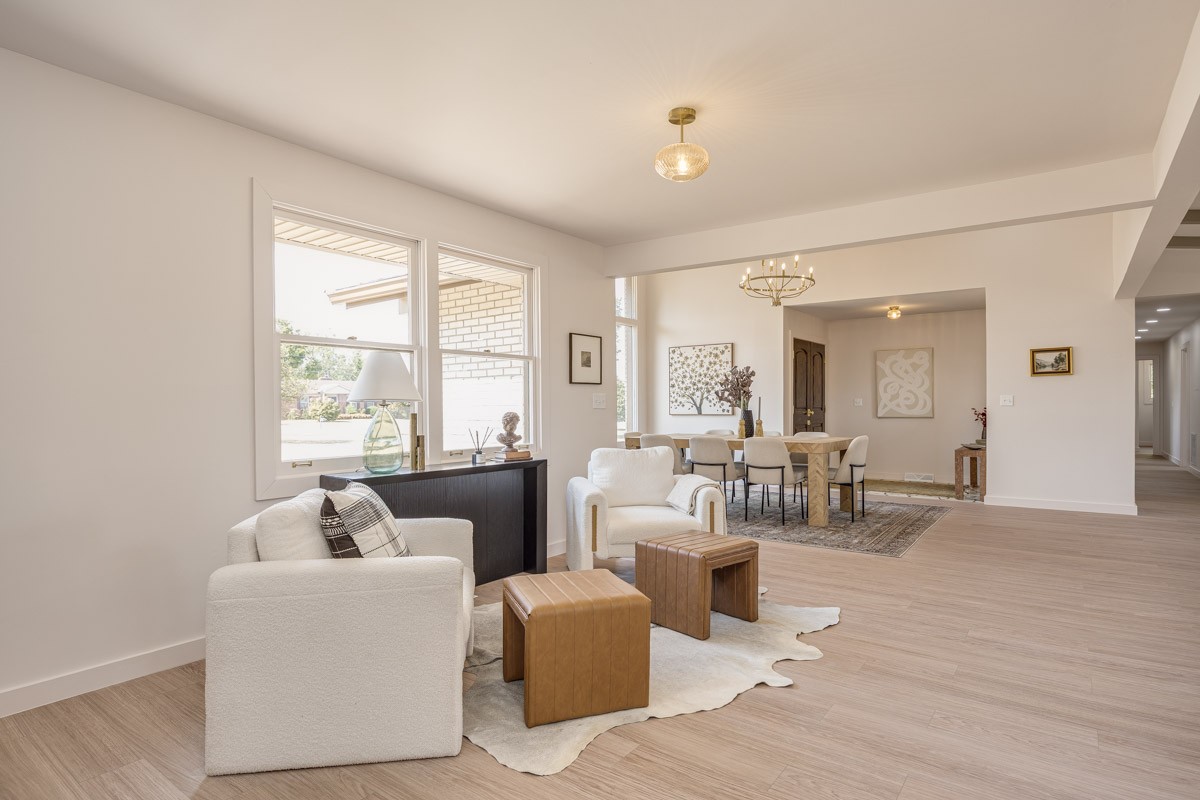 Open-plan living and dining room with white armchairs, leather ottomans, and large windows.
